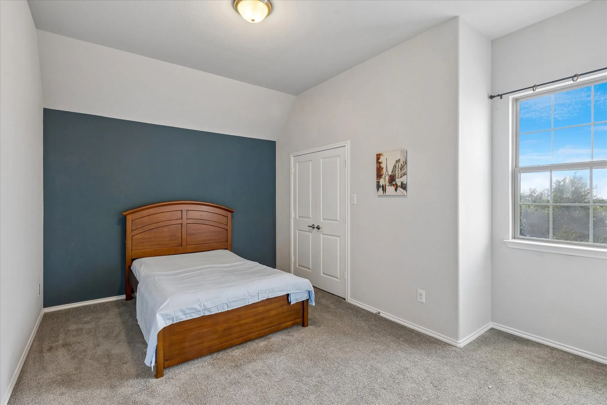 Bedroom featuring a prominent dark accent wall, soft gray carpeting, and a window with a clear sky backdrop