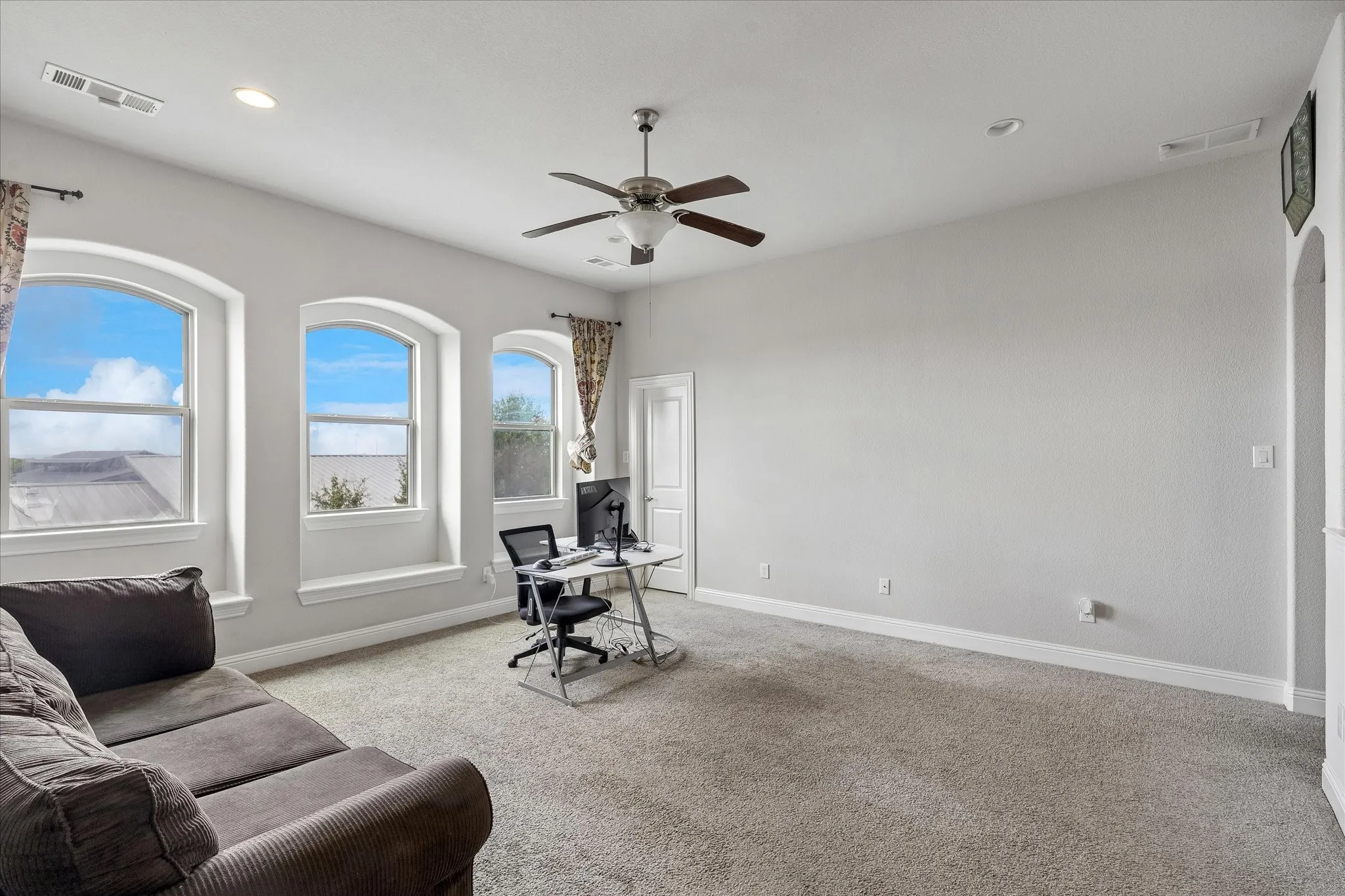 Spacious room featuring three arched windows with sills, neutral carpeting, a ceiling fan, and recessed lighting