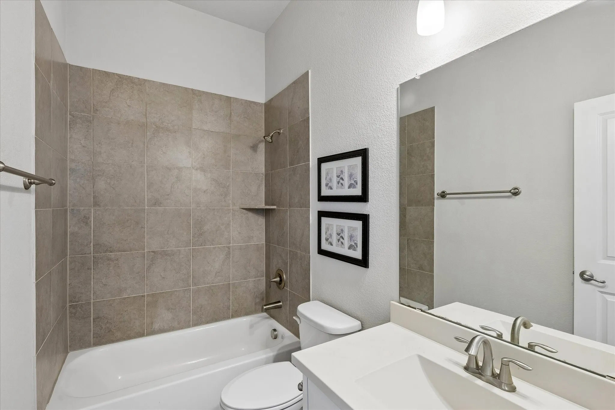Full bathroom featuring a white tub, light-toned wall tiling, a built-in shower shelf, brushed nickel fixtures, and a white vanity with an integrated sink