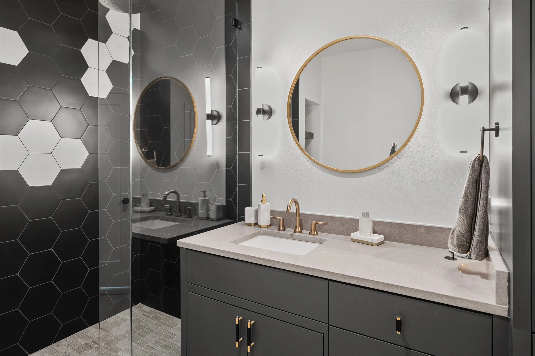 Contemporary bathroom featuring a dark vanity with gold-tone hardware, an integrated sink, and a light-toned countertop