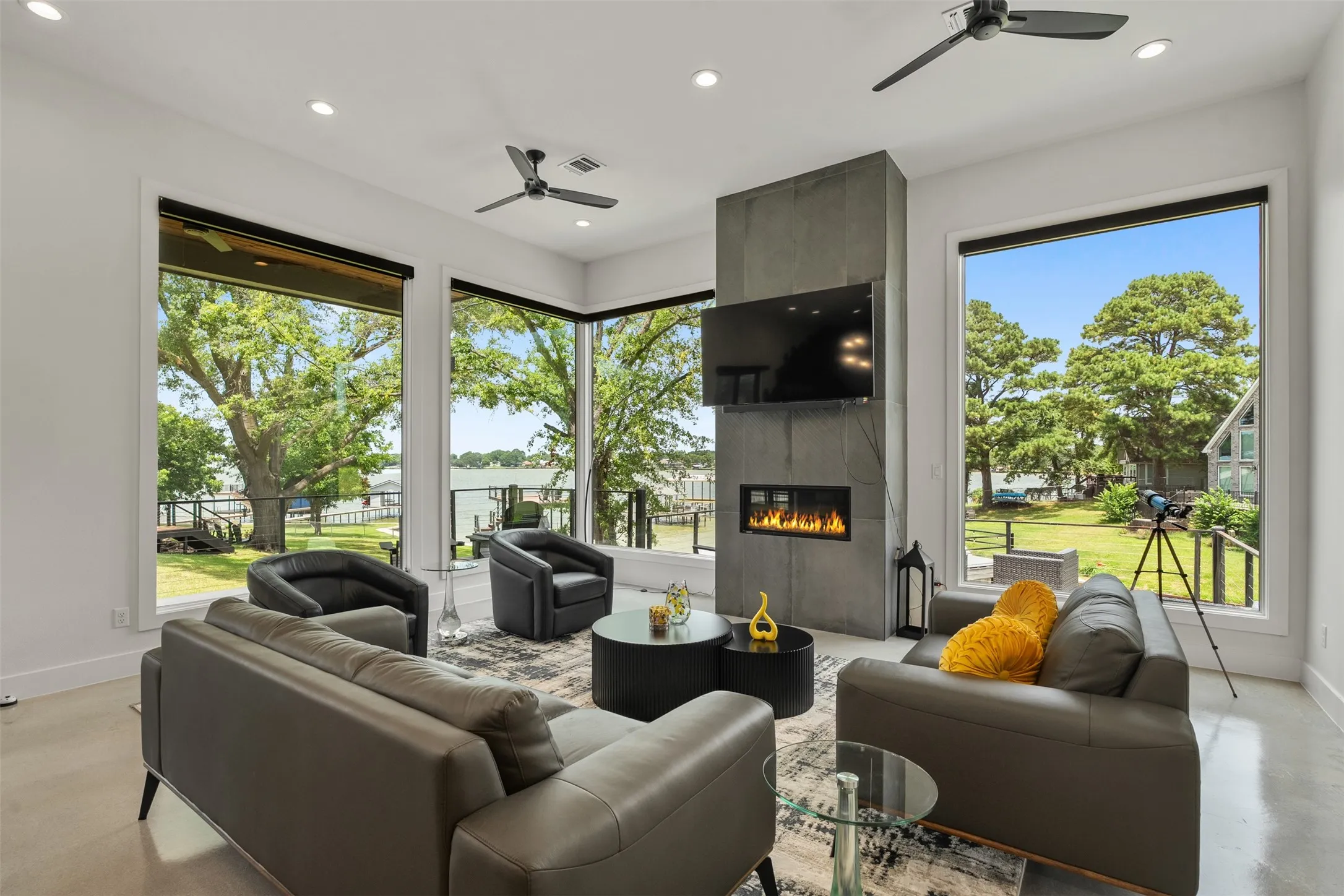 Living space featuring expansive windows, a contemporary electric fireplace with a stone-finish surround, recessed lighting, and ceiling fans
