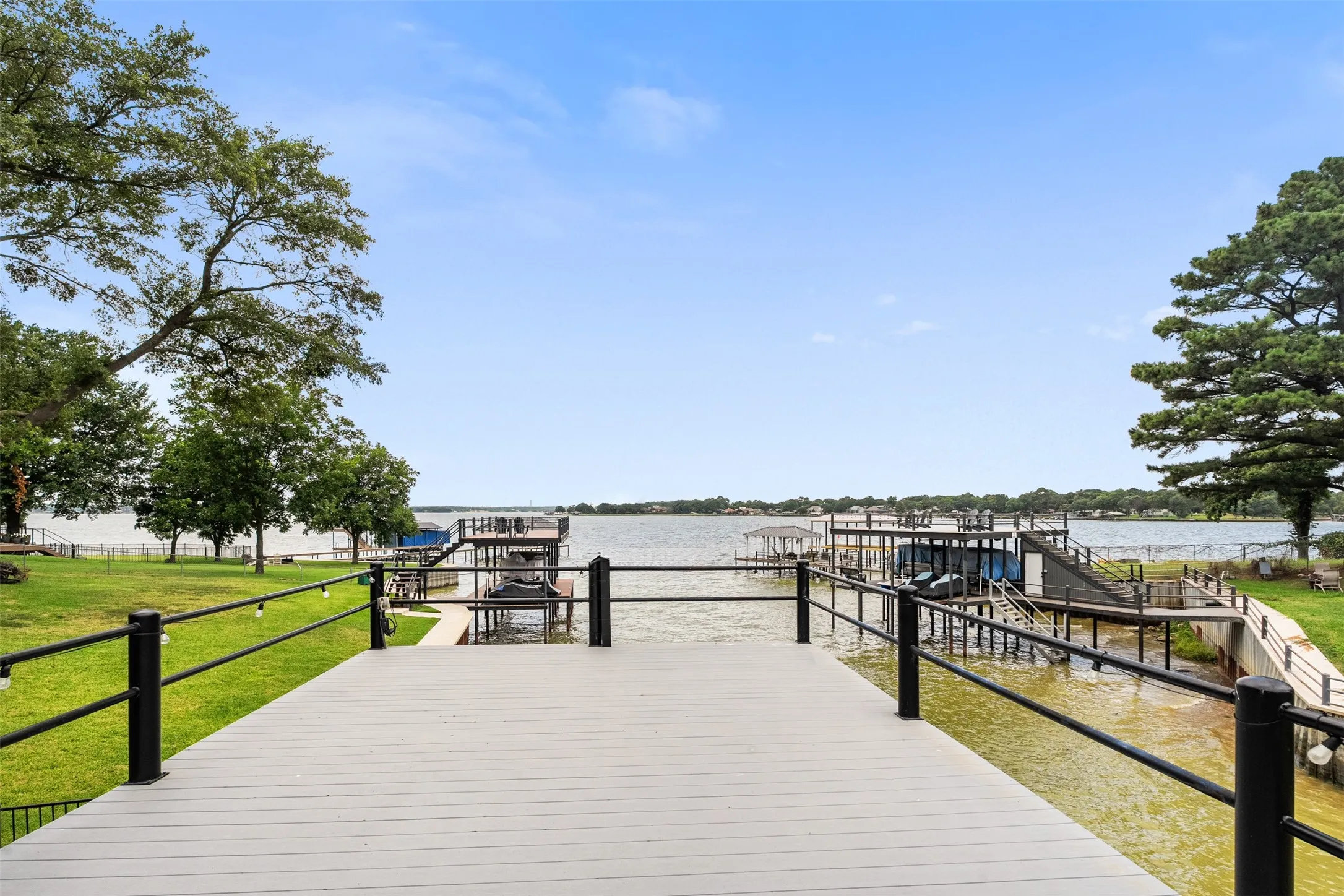 Waterfront property featuring a spacious dock with integrated boat slips, composite decking, black metal railings, and a manicured lawn
