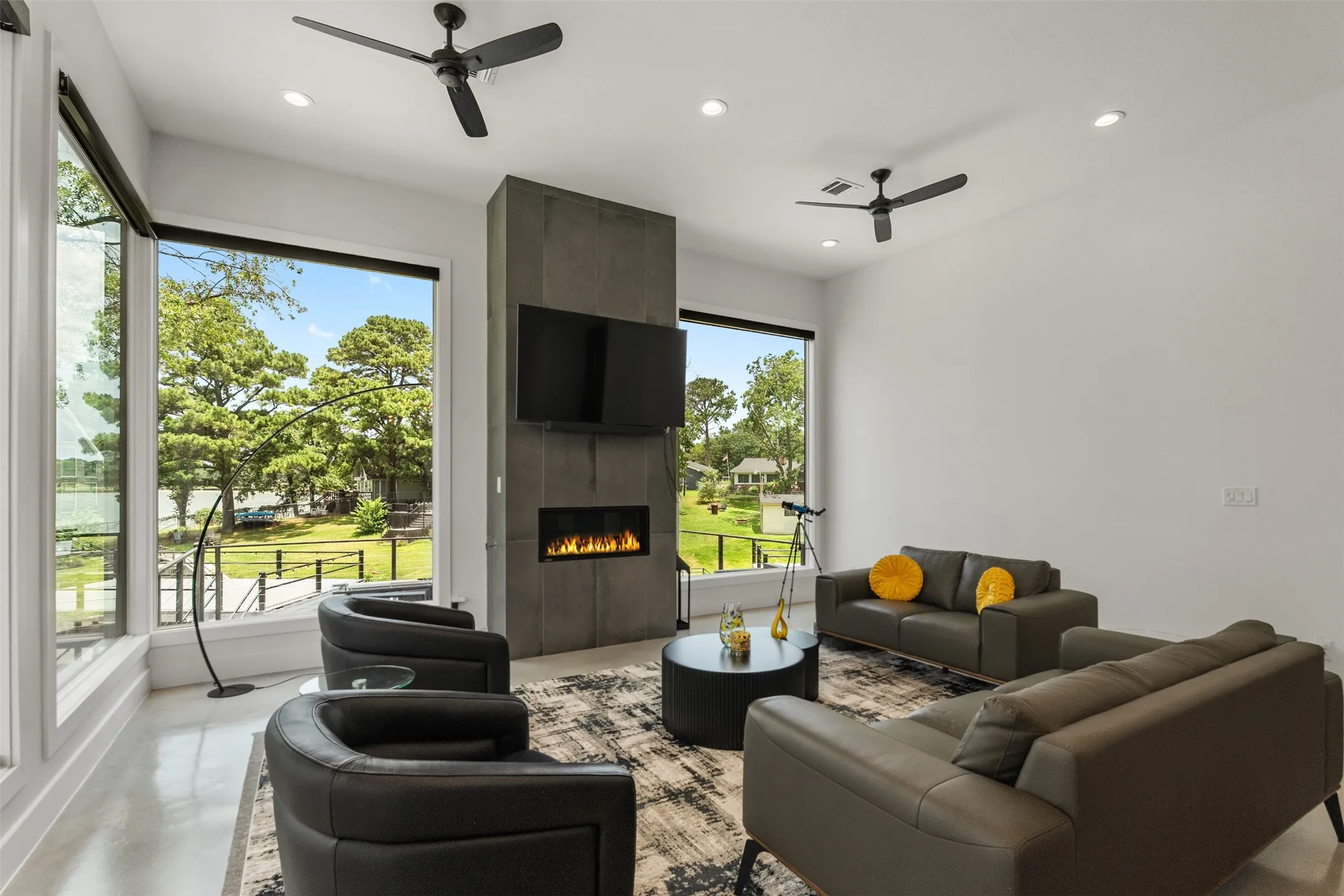 Expansive living space featuring full-height windows, a contemporary fireplace with a mounted television, and recessed lighting