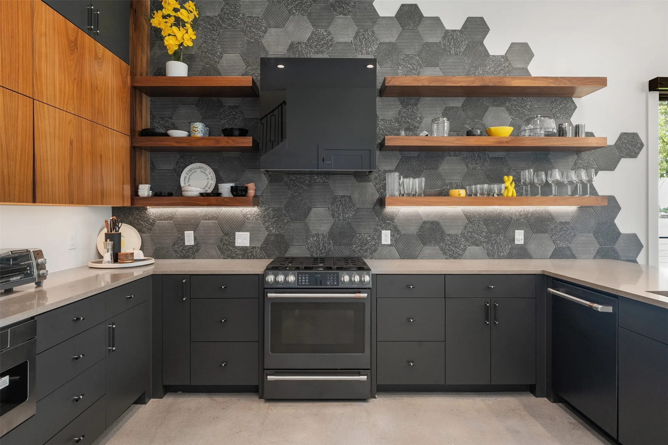Contemporary kitchen with dark lower cabinetry, light wood-finish upper cabinetry, and a full suite of black appliances