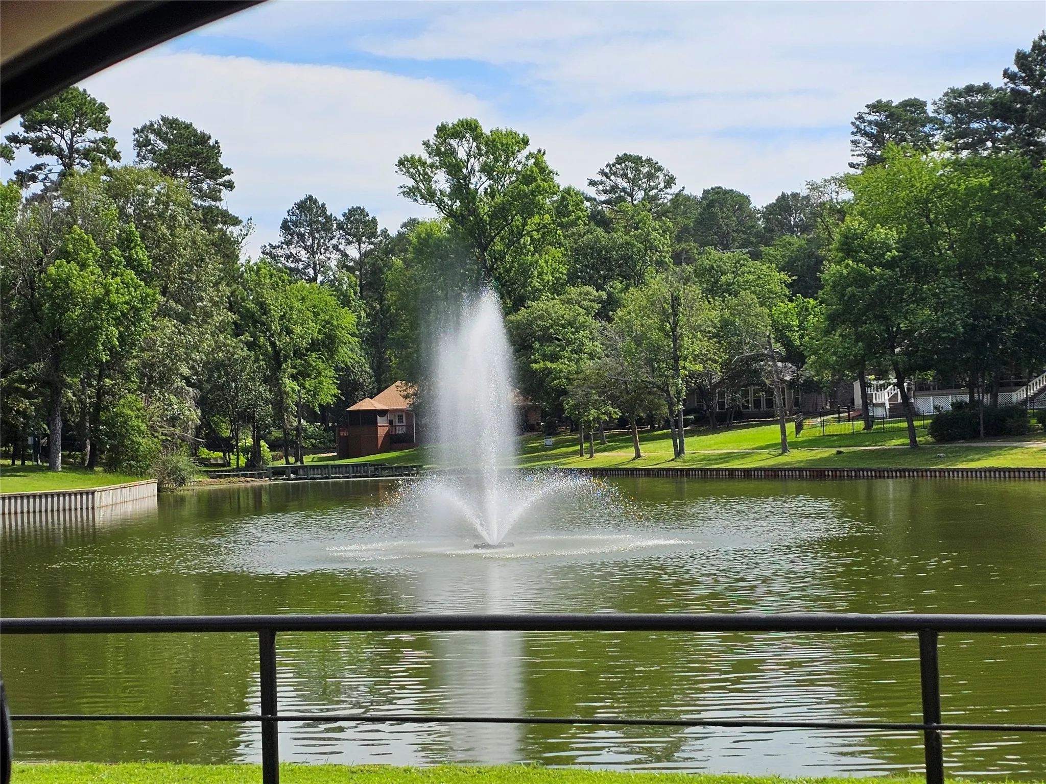 Tranquil lake featuring a central fountain, surrounded by lush green trees and a manicured shoreline