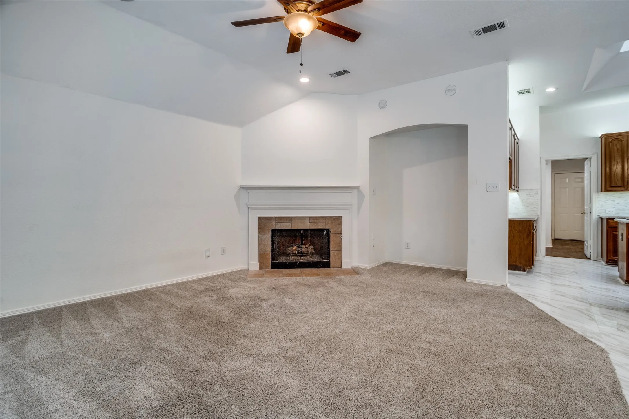Unfurnished living room featuring a ceiling fan, light carpet, a fireplace, and lofted ceiling