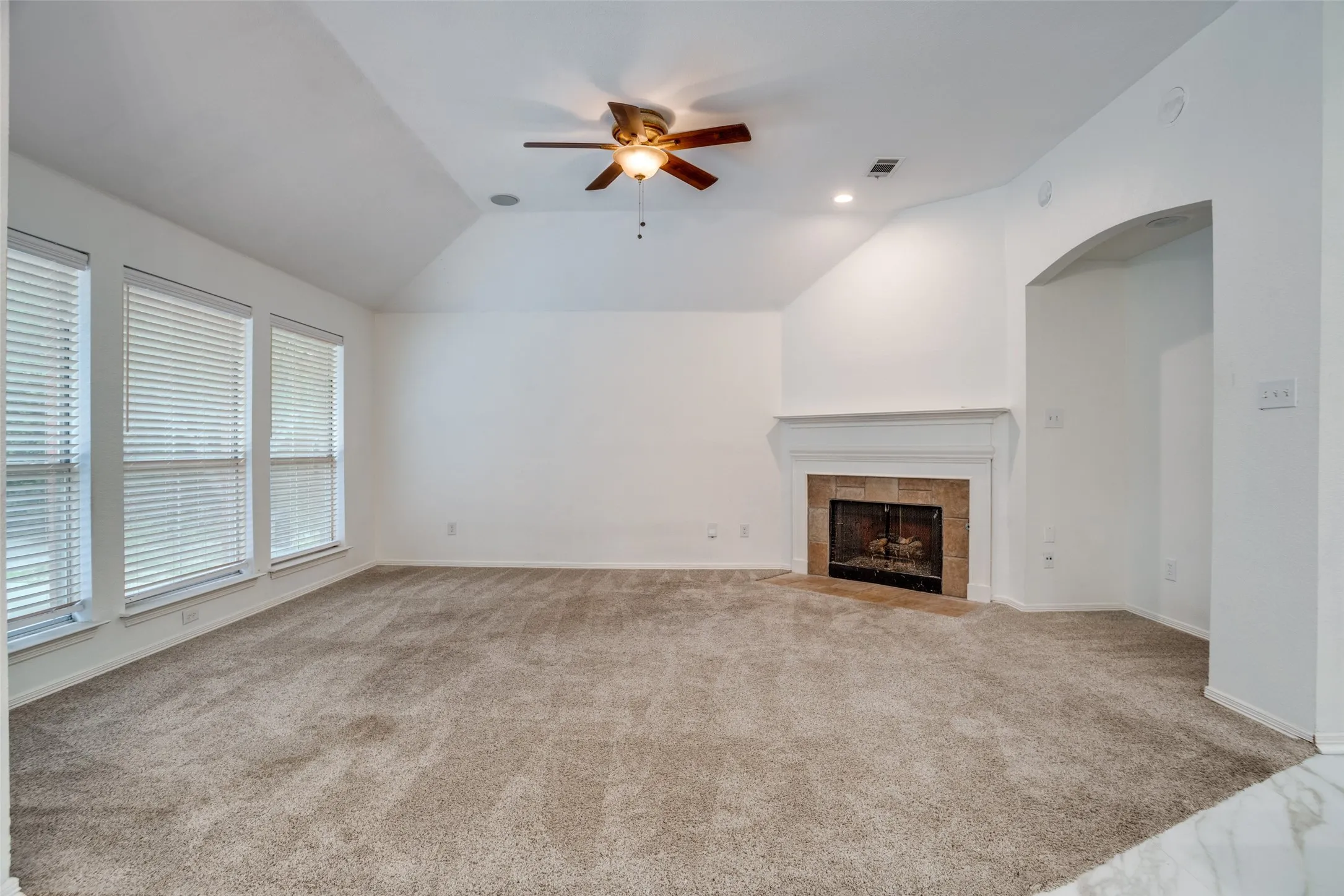 Unfurnished living room with a ceiling fan, light carpet, vaulted ceiling, and a fireplace
