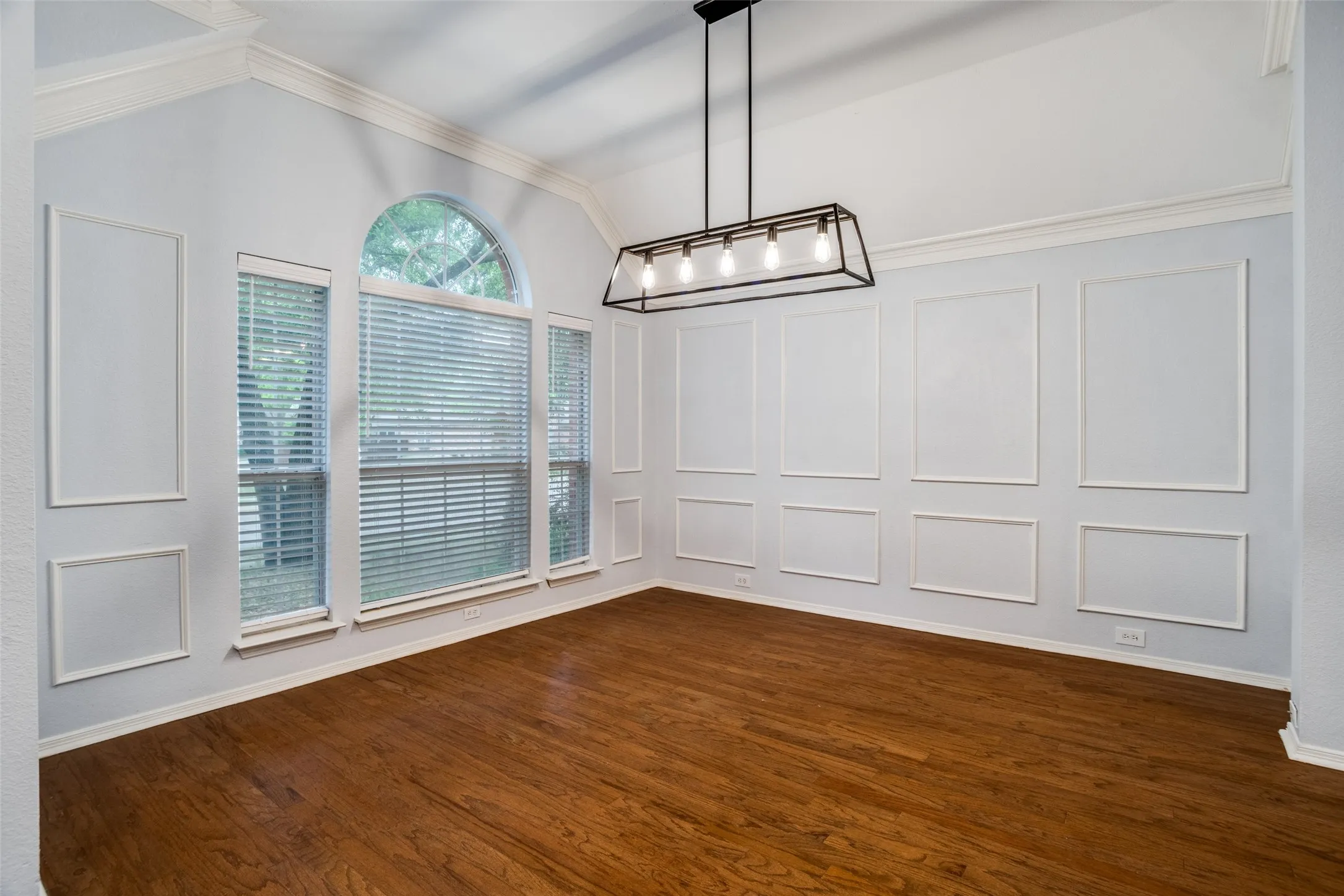 Unfurnished dining area with a decorative wall, vaulted ceiling, a chandelier, dark wood-type flooring, and crown molding