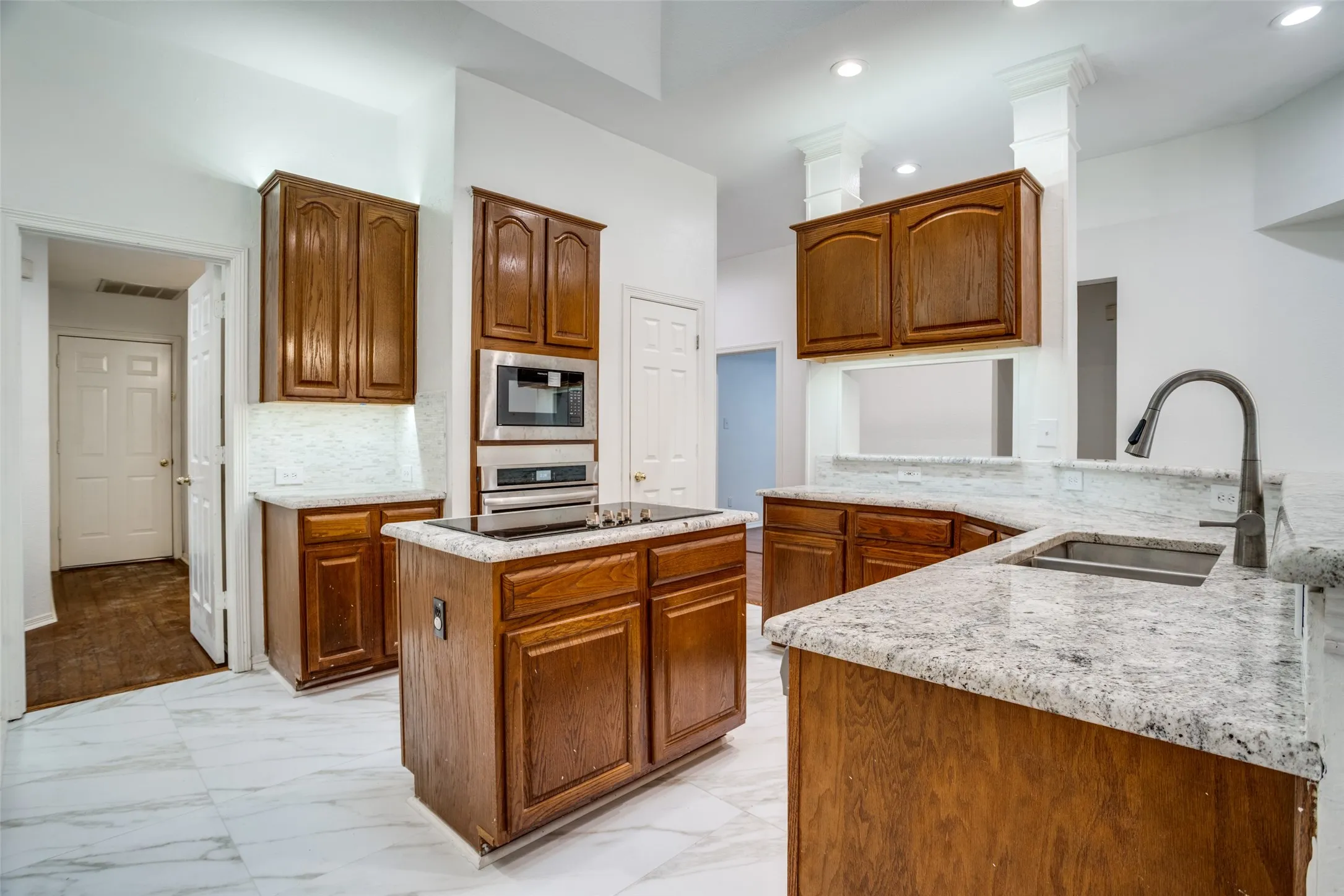 Kitchen featuring wood finish cabinets, a center island, light marble finish floors, light stone counters, and recessed lighting