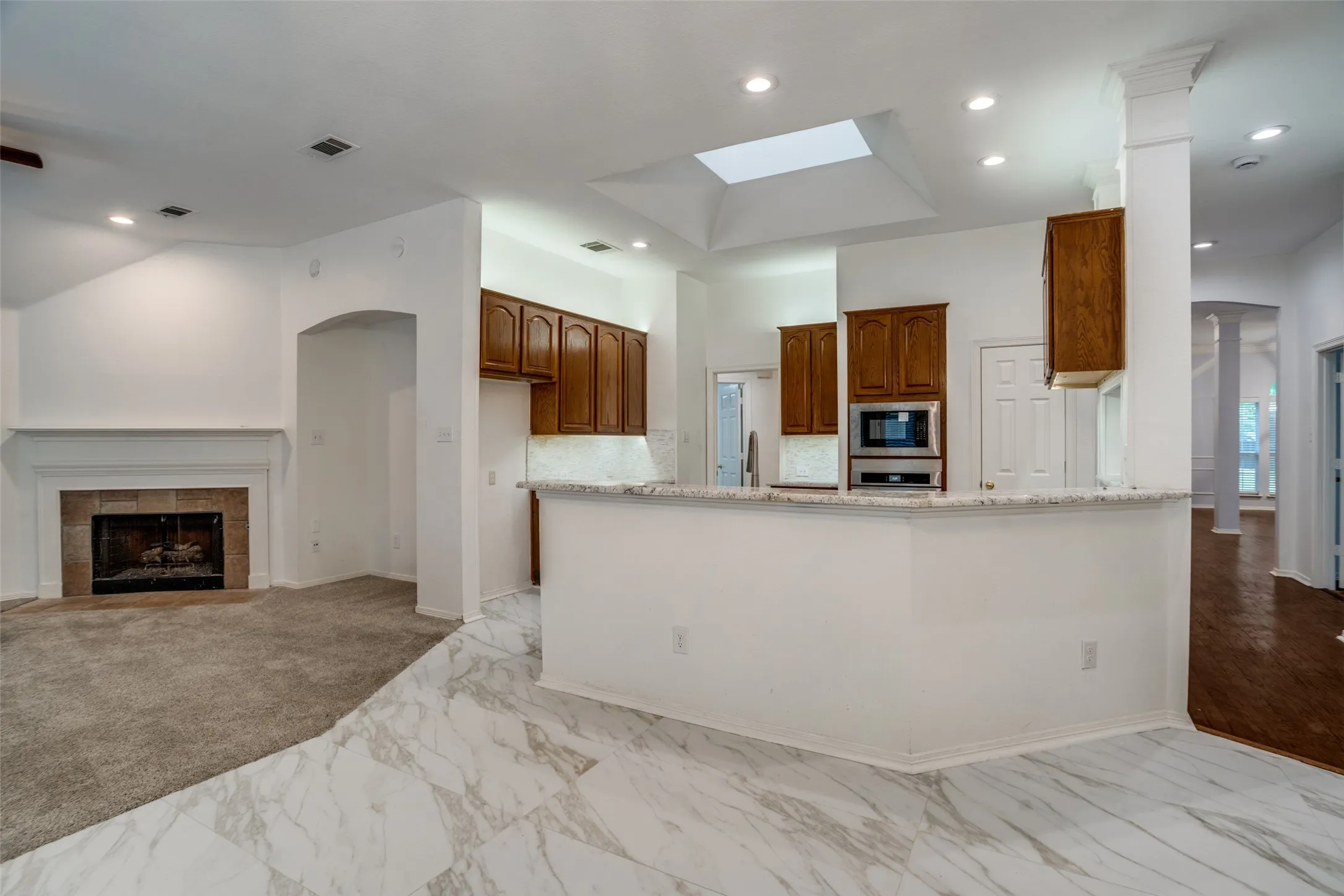 Kitchen featuring open floor plan, a peninsula, wood finish cabinetry, decorative columns, and light marble finish flooring