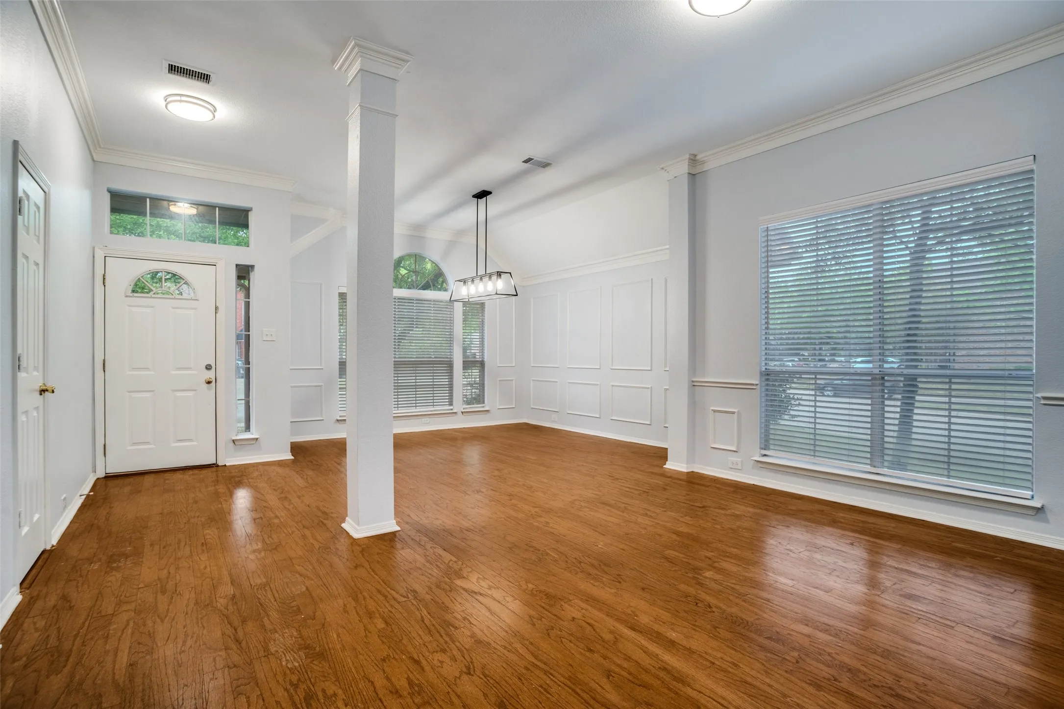 Foyer entrance with a decorative wall, ornate columns, crown molding, dark wood-style flooring, and suspended lighting