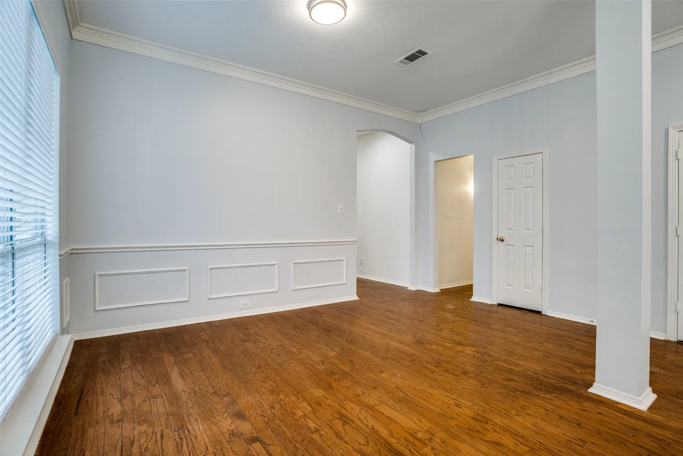 Unfurnished room with arched walkways, crown molding, dark wood-style flooring, wainscoting, and a decorative wall