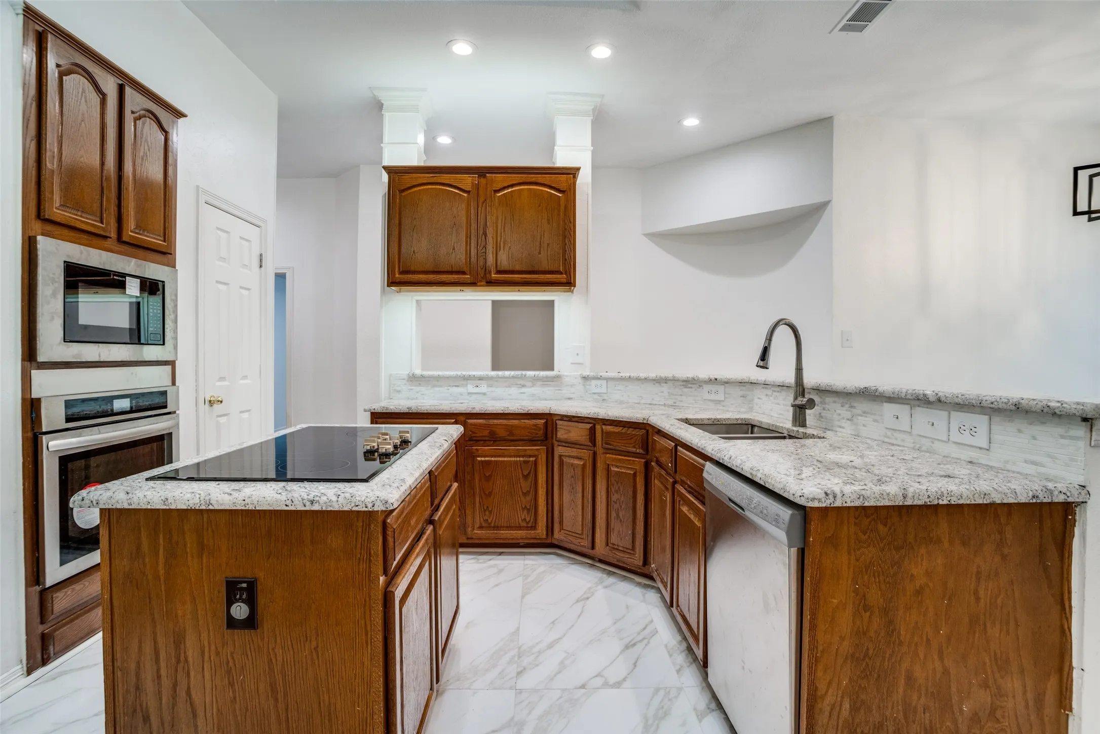 Kitchen with light marble finish flooring, stainless steel appliances, a kitchen island, light stone counters, and wood finish cabinets