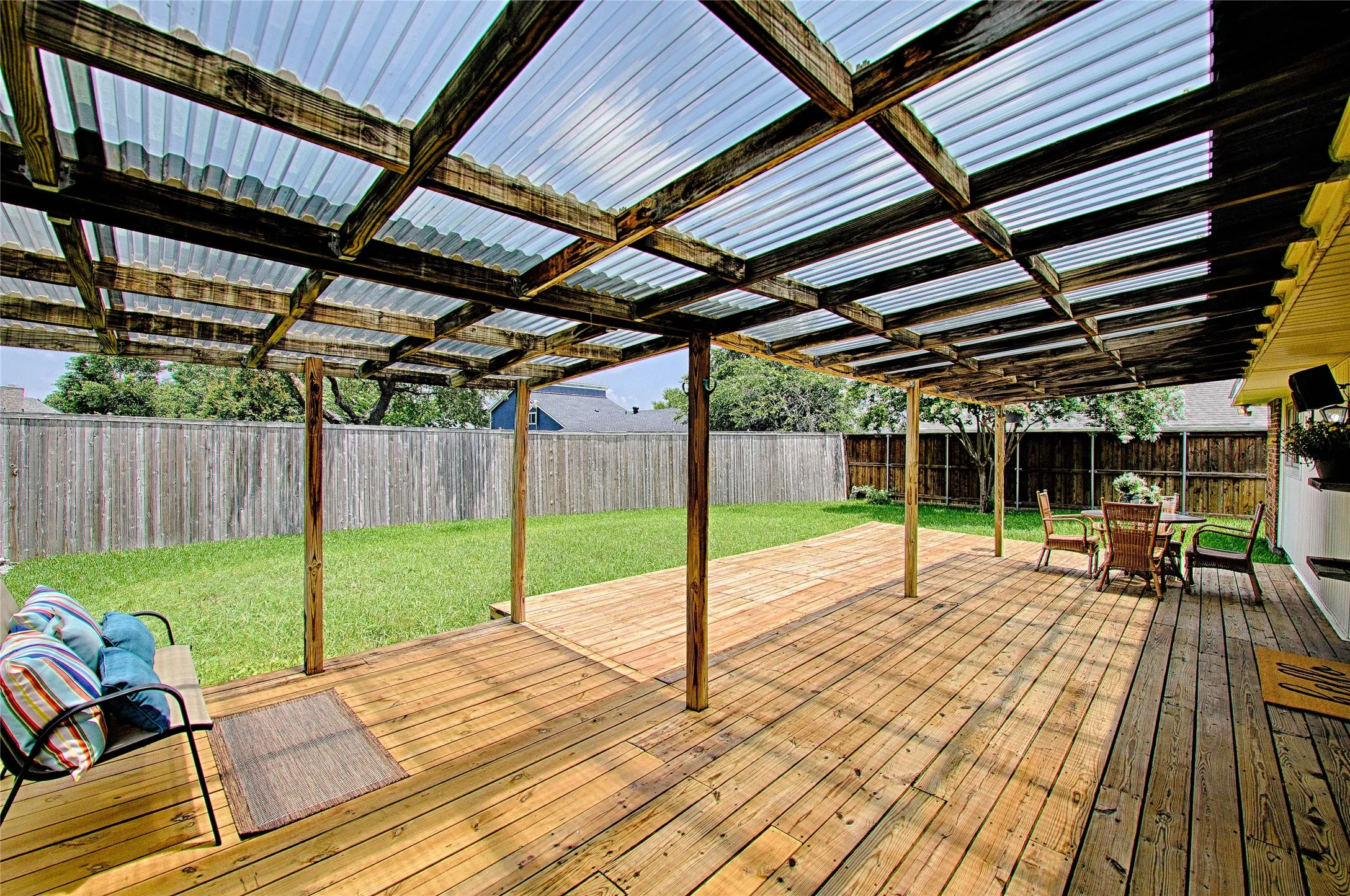 Expansive backyard featuring a wood deck, partial clear panel roof, and a privacy fence