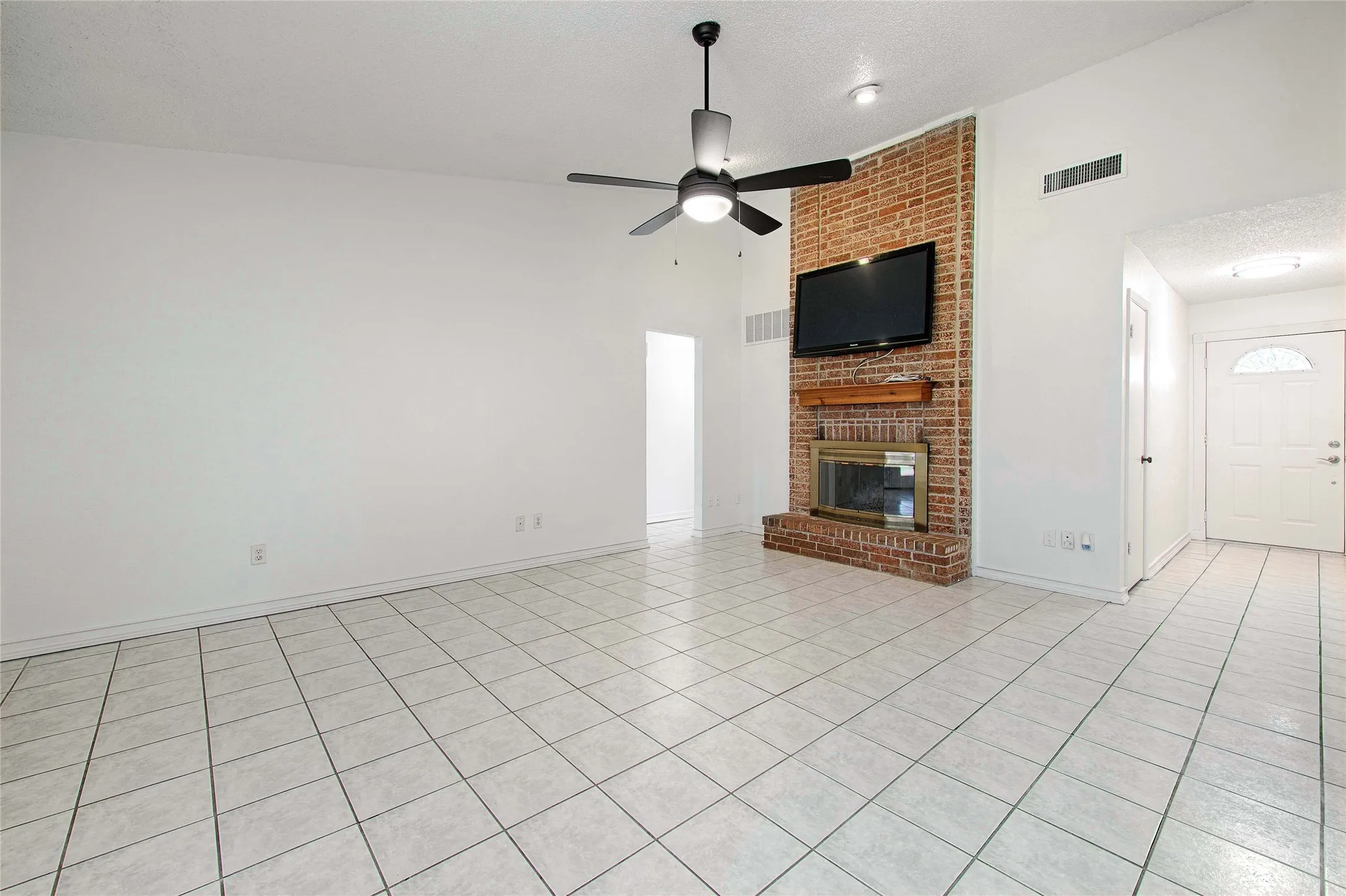 Living area featuring a brick fireplace with a wood mantle, a ceiling fan, and tile flooring