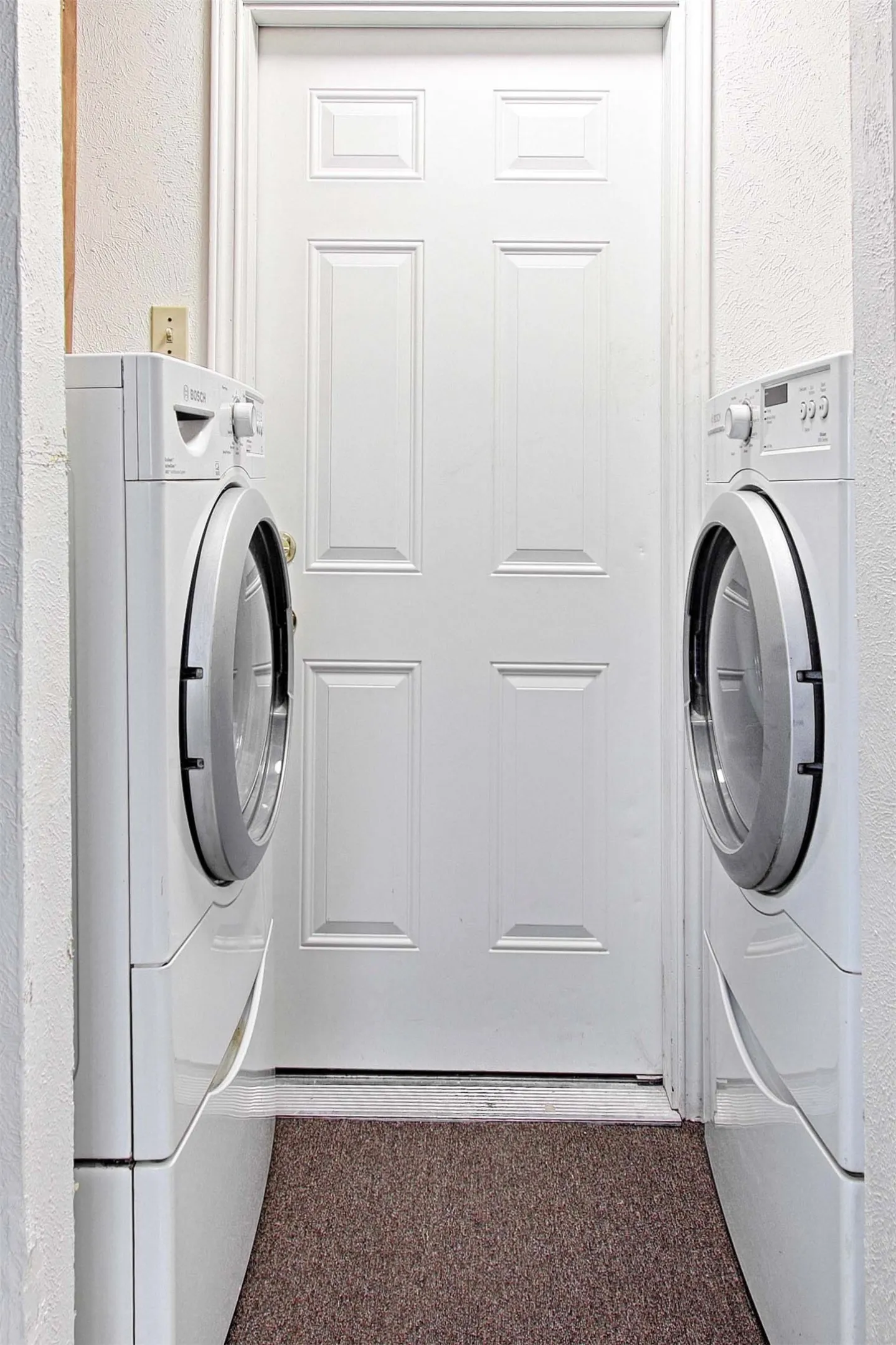 Dedicated laundry area featuring a paneled door, textured walls, and a textured floor covering