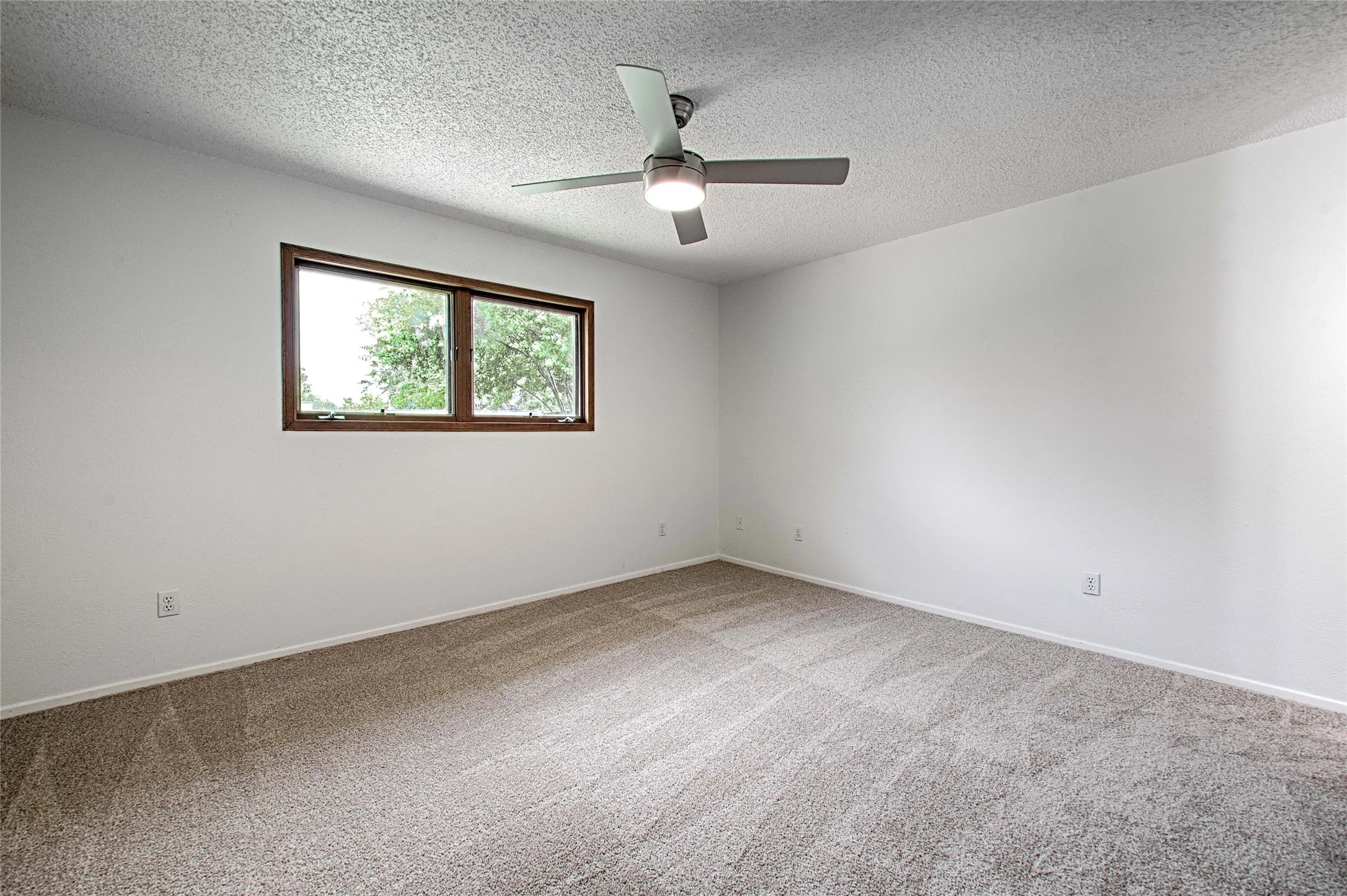 Expansive room with neutral carpeting and a modern ceiling fan with integrated lighting