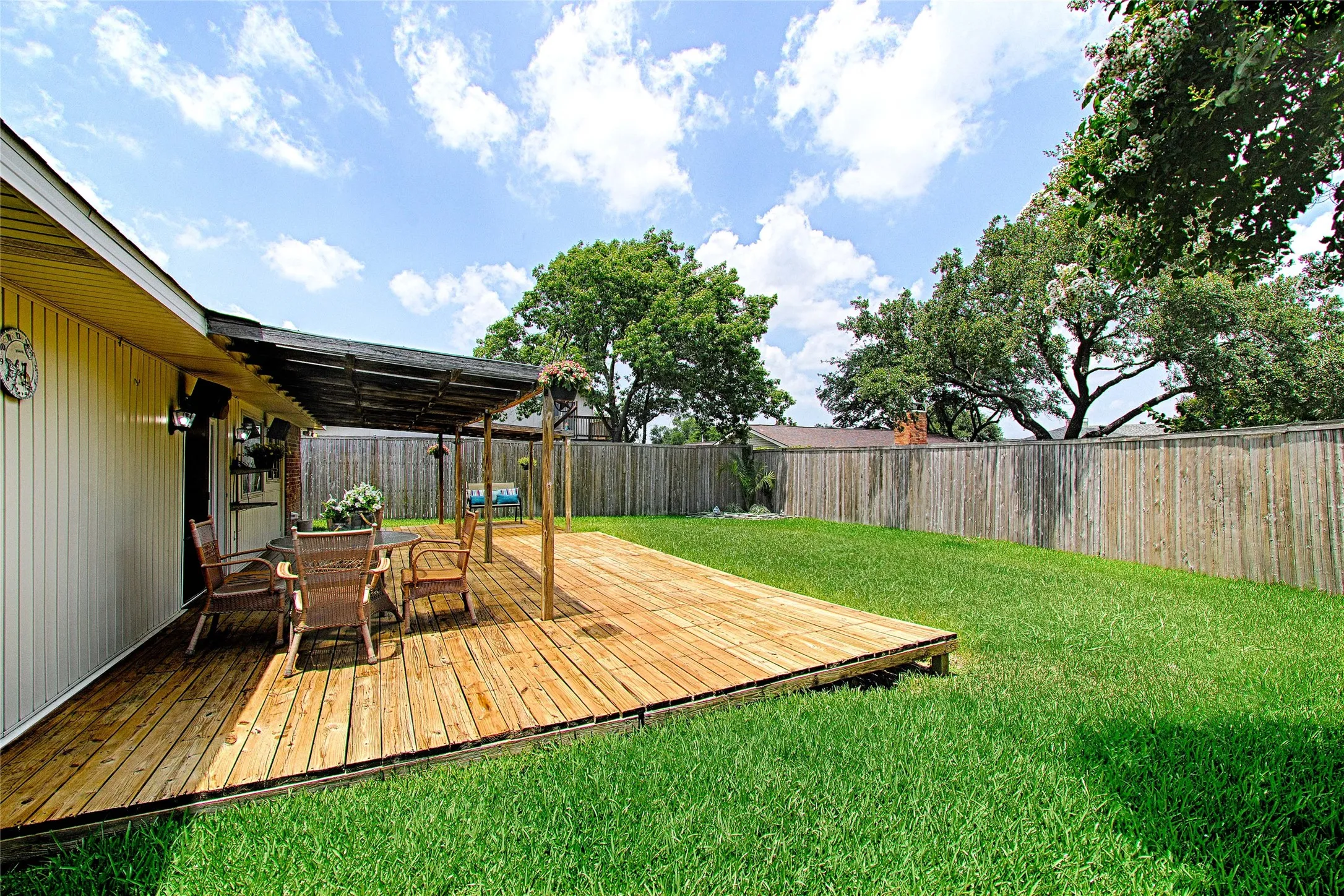 Expansive backyard featuring a large wooden deck with a shaded pergola, a manicured lawn, and a perimeter wood privacy fence