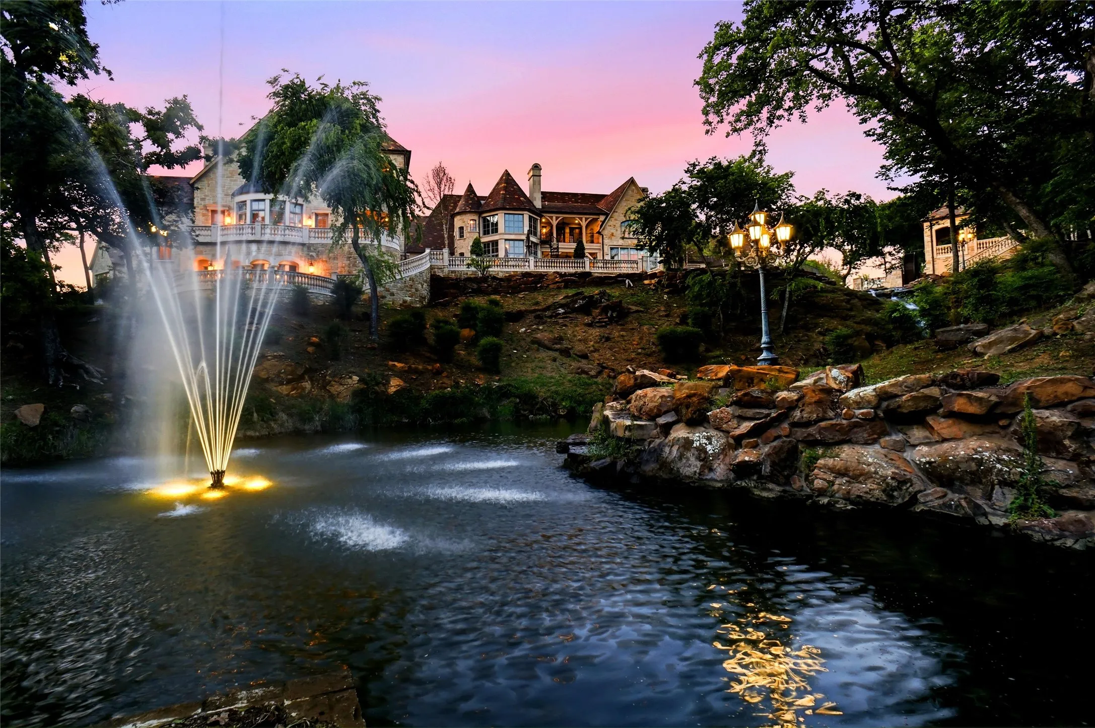 Illuminated water feature with a lighted fountain set against a hillside property