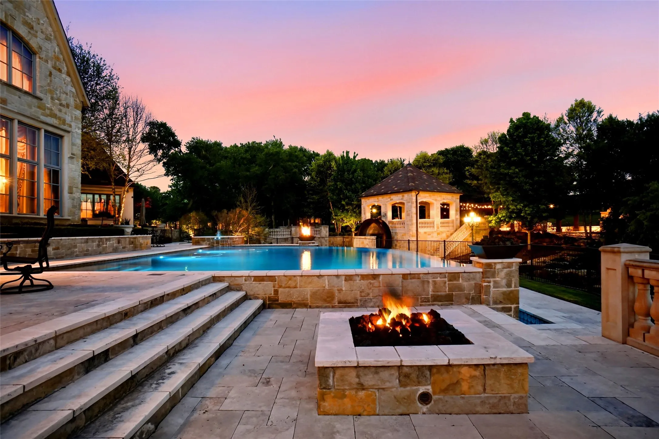 Outdoor living area featuring a built-in stone fire pit, extensive stone patio, and a swimming pool with integrated lighting
