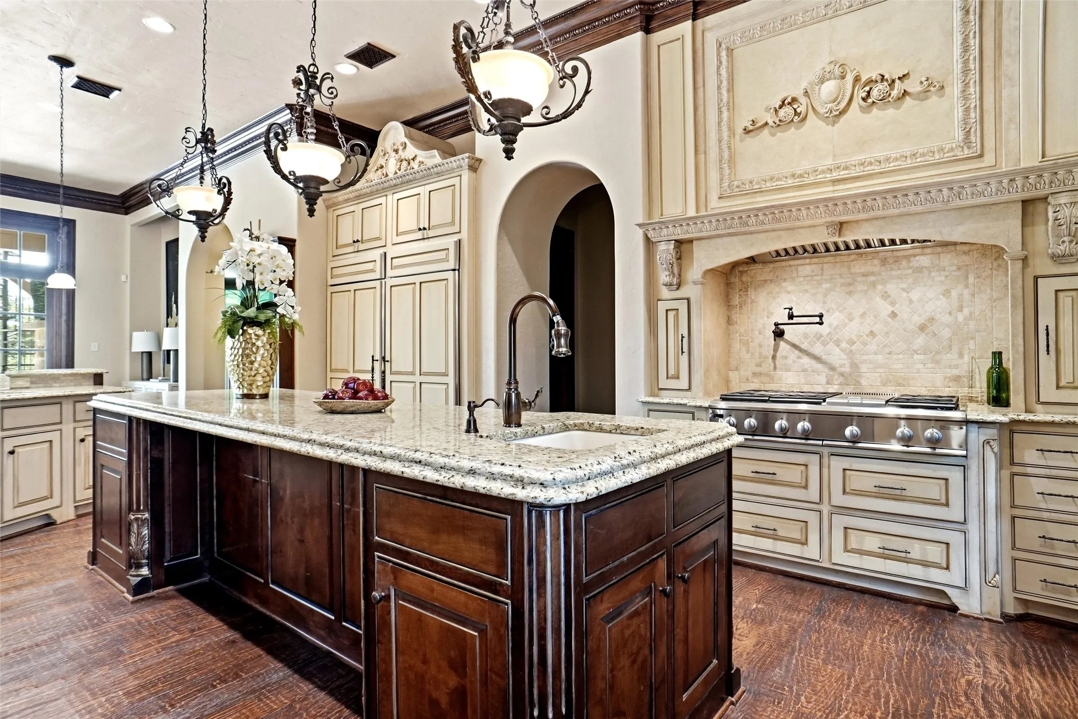 Gourmet kitchen featuring an oversized island with an integrated sink, granite countertops, and rich wood-finish flooring