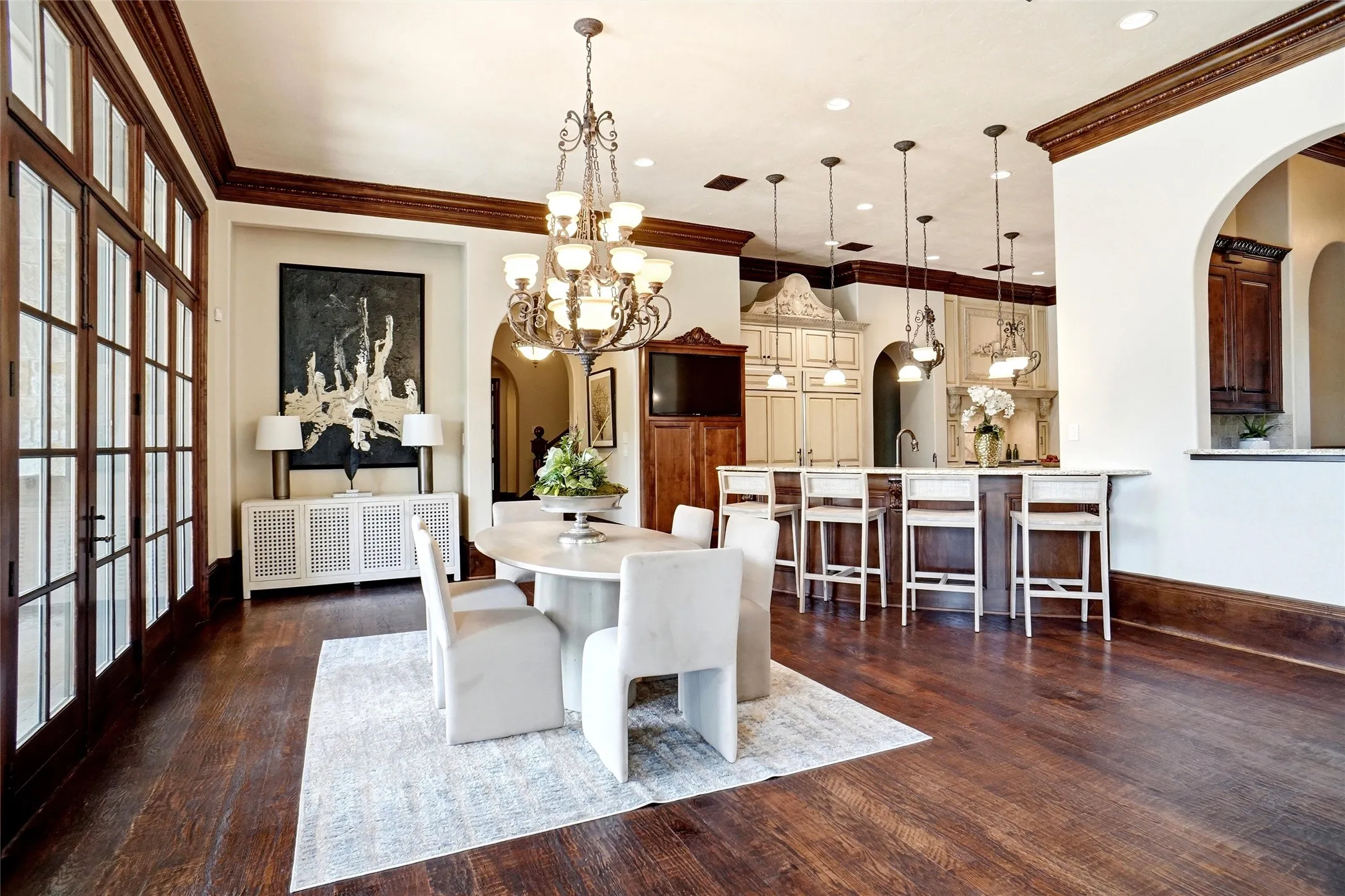 Spacious dining area featuring dark wood-finish flooring, a multi-tier chandelier, and broad French doors leading to the covered patio space.