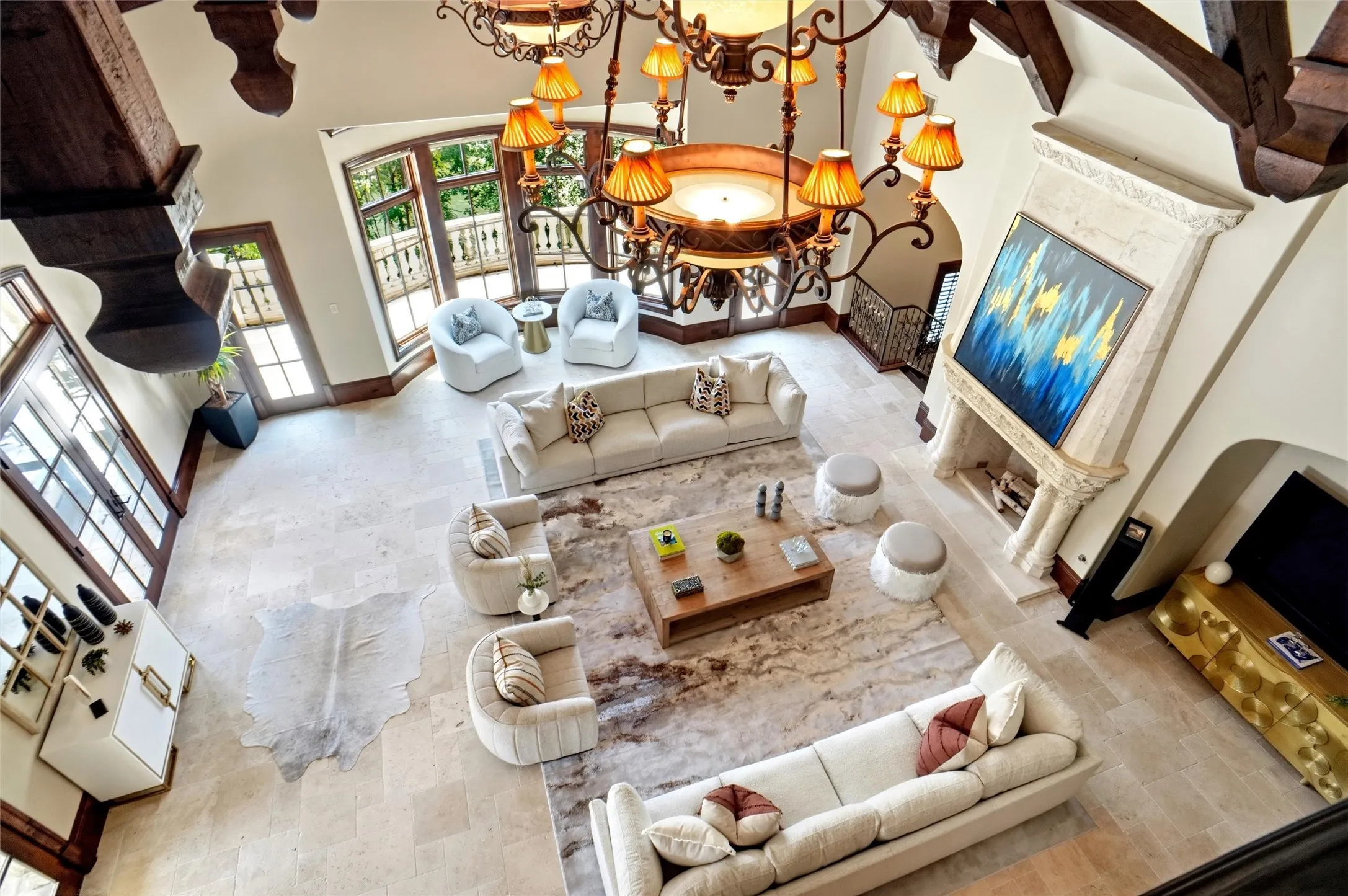 Located in the additional home side. Spacious second great room featuring a grand chandelier, exposed wood beam ceilings, a carved stone fireplace, and multiple sets of French doors. This view is looking over the Juliet balcony down.