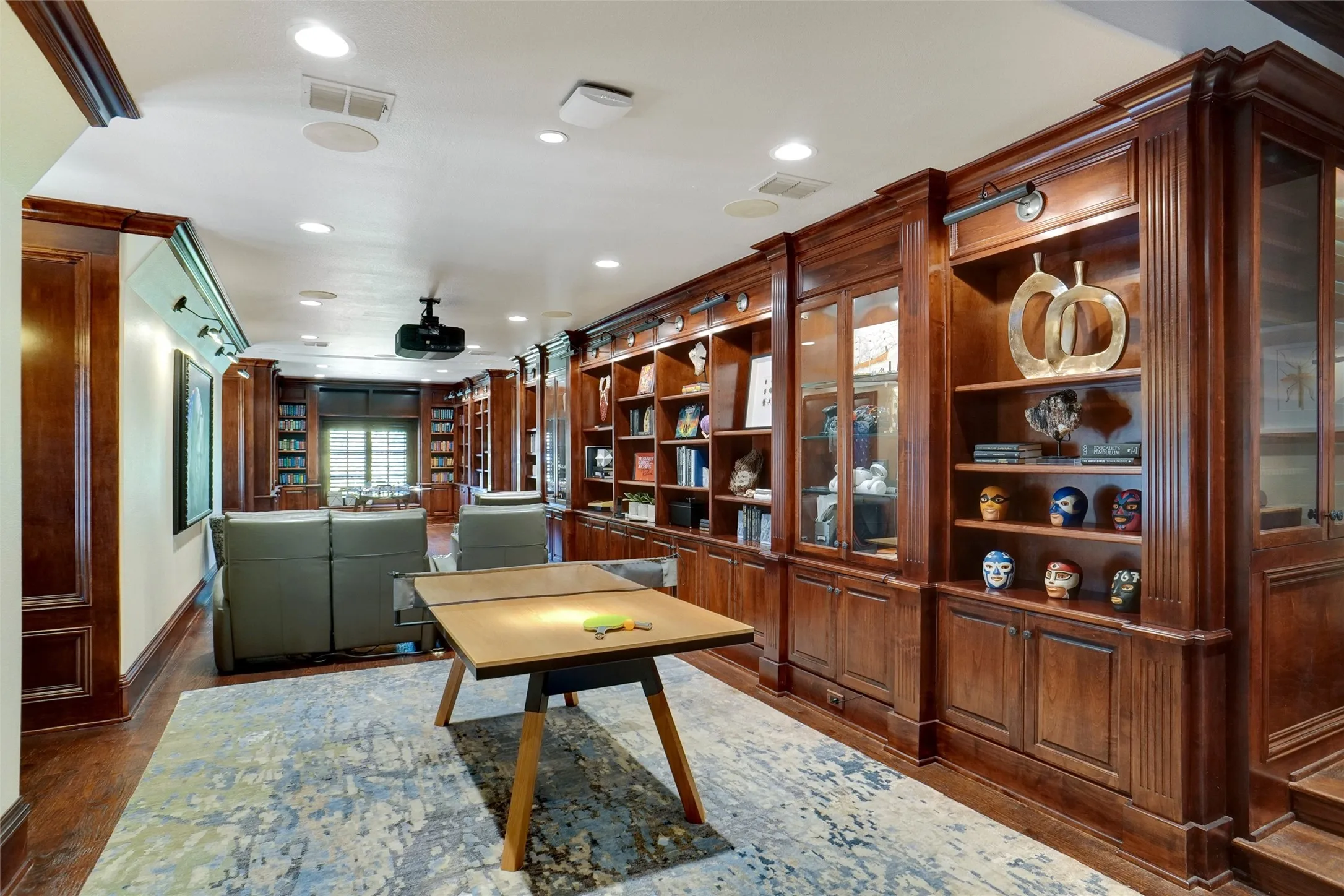 Custom built-in wood cabinetry and shelving feature glass-front display cases and detailed millwork, complemented by a concealed motorized movie screen that retracts into the ceiling.