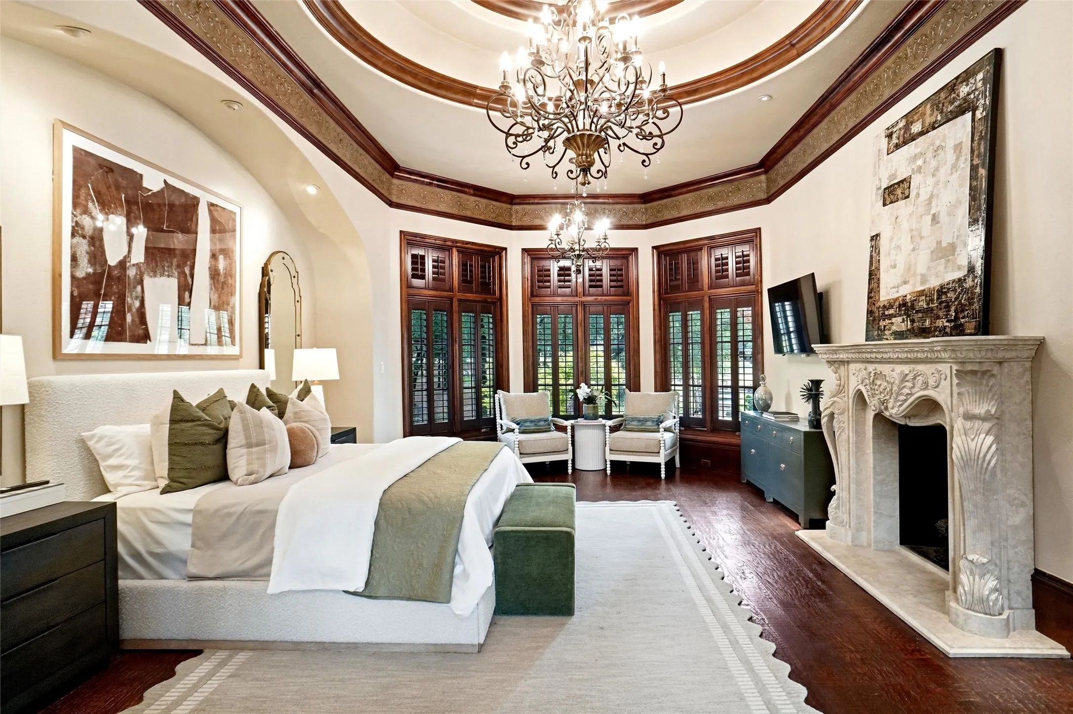 Spacious interior featuring a decorative coffered ceiling with a chandelier, wood-finish flooring, a detailed stone fireplace, and multiple windows with interior wood shutters