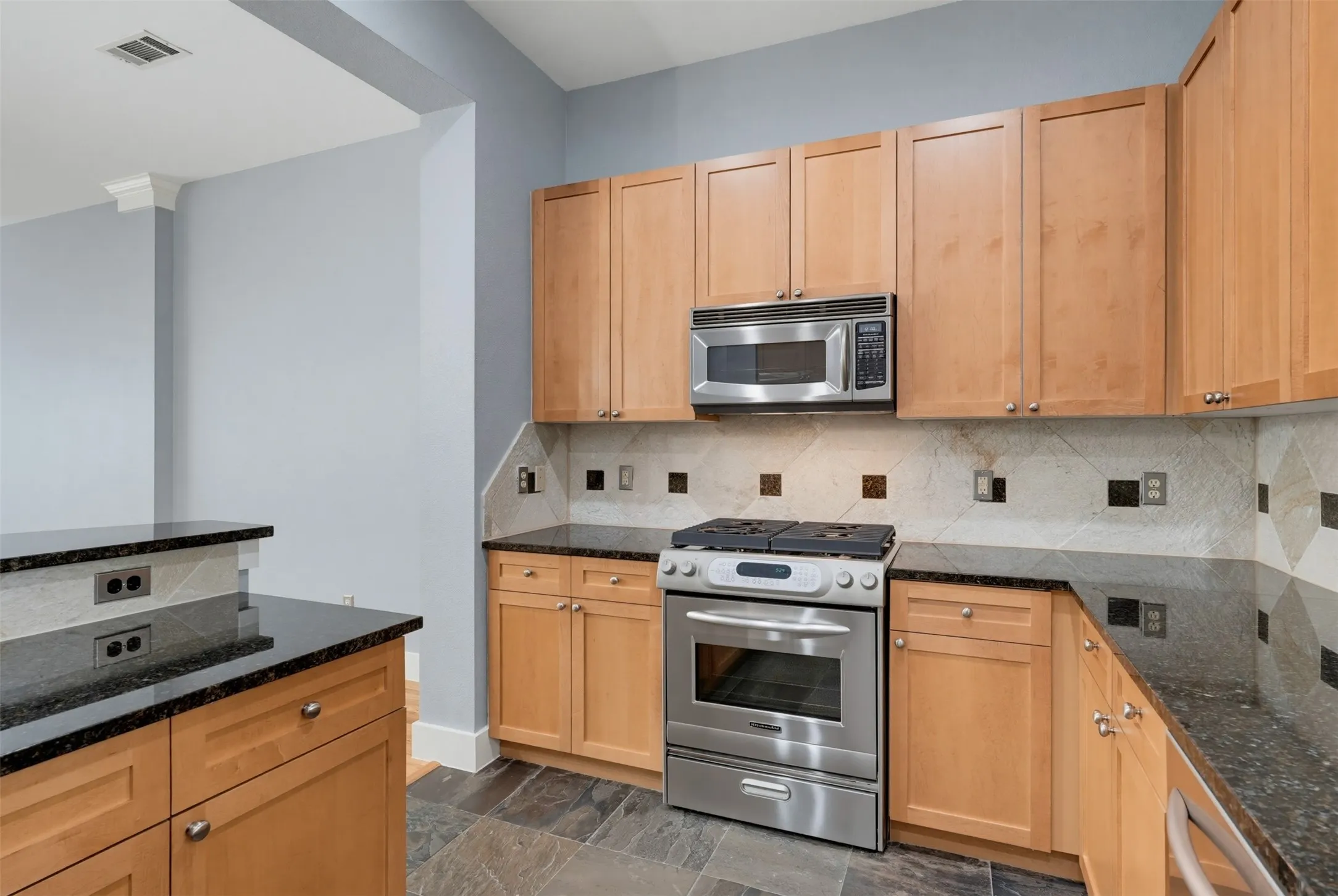 Kitchen featuring wood-finish cabinetry, black stone countertops, stainless steel appliances, and a decorative tile backsplash