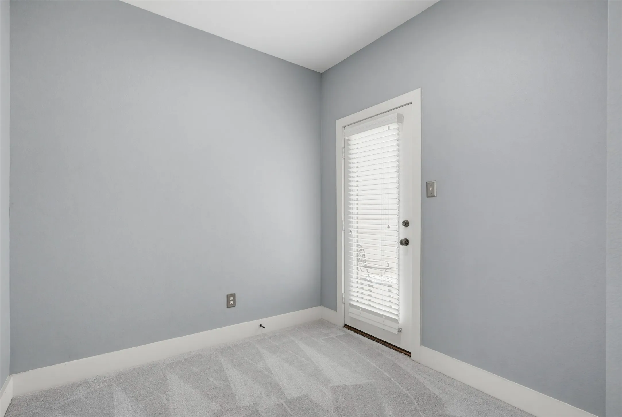 Light gray walls complemented by white baseboards, plush gray patterned carpeting, and a white door featuring integrated blinds