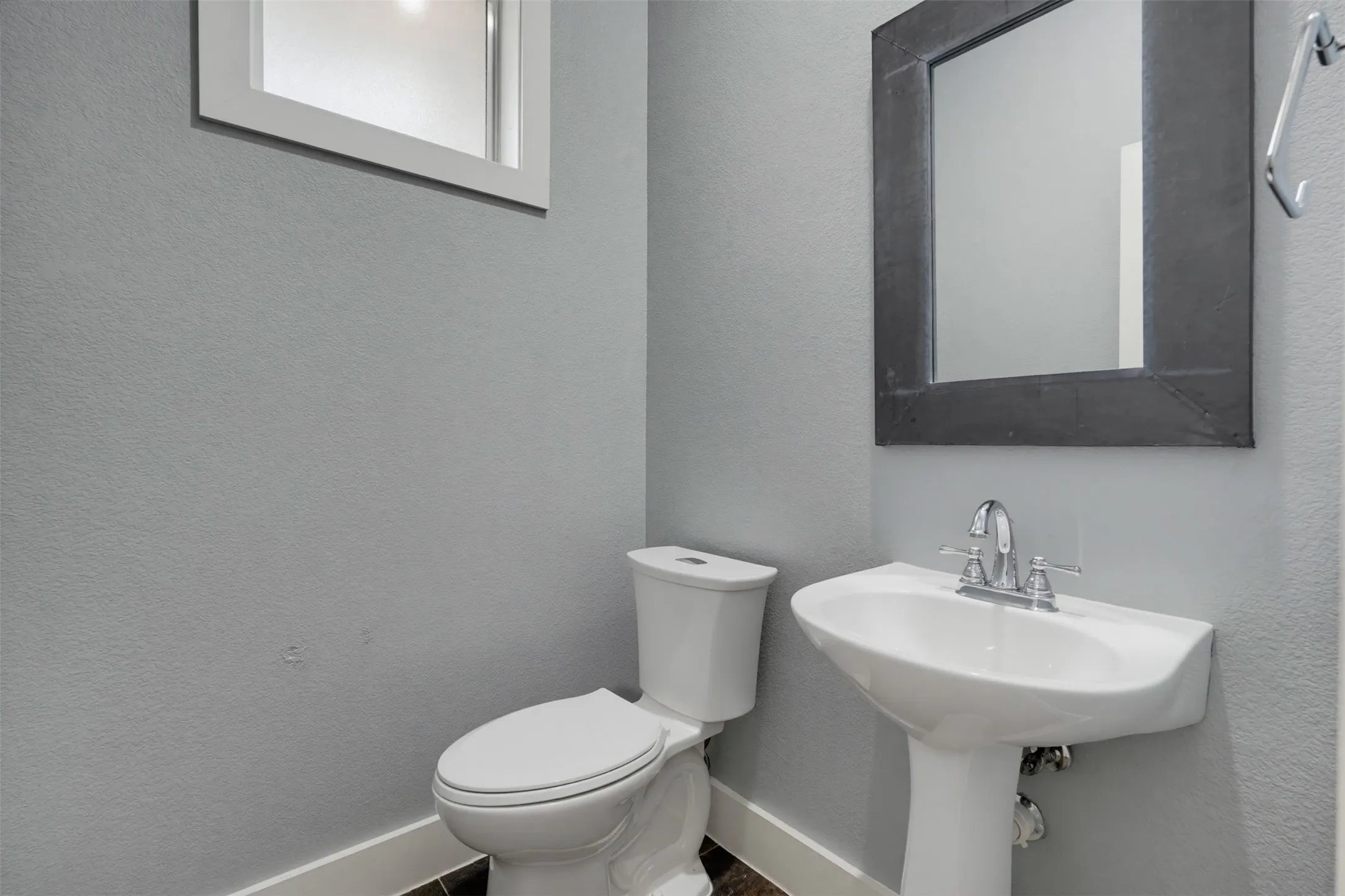 Pedestal sink with chrome faucet, white toilet, and dark framed mirror