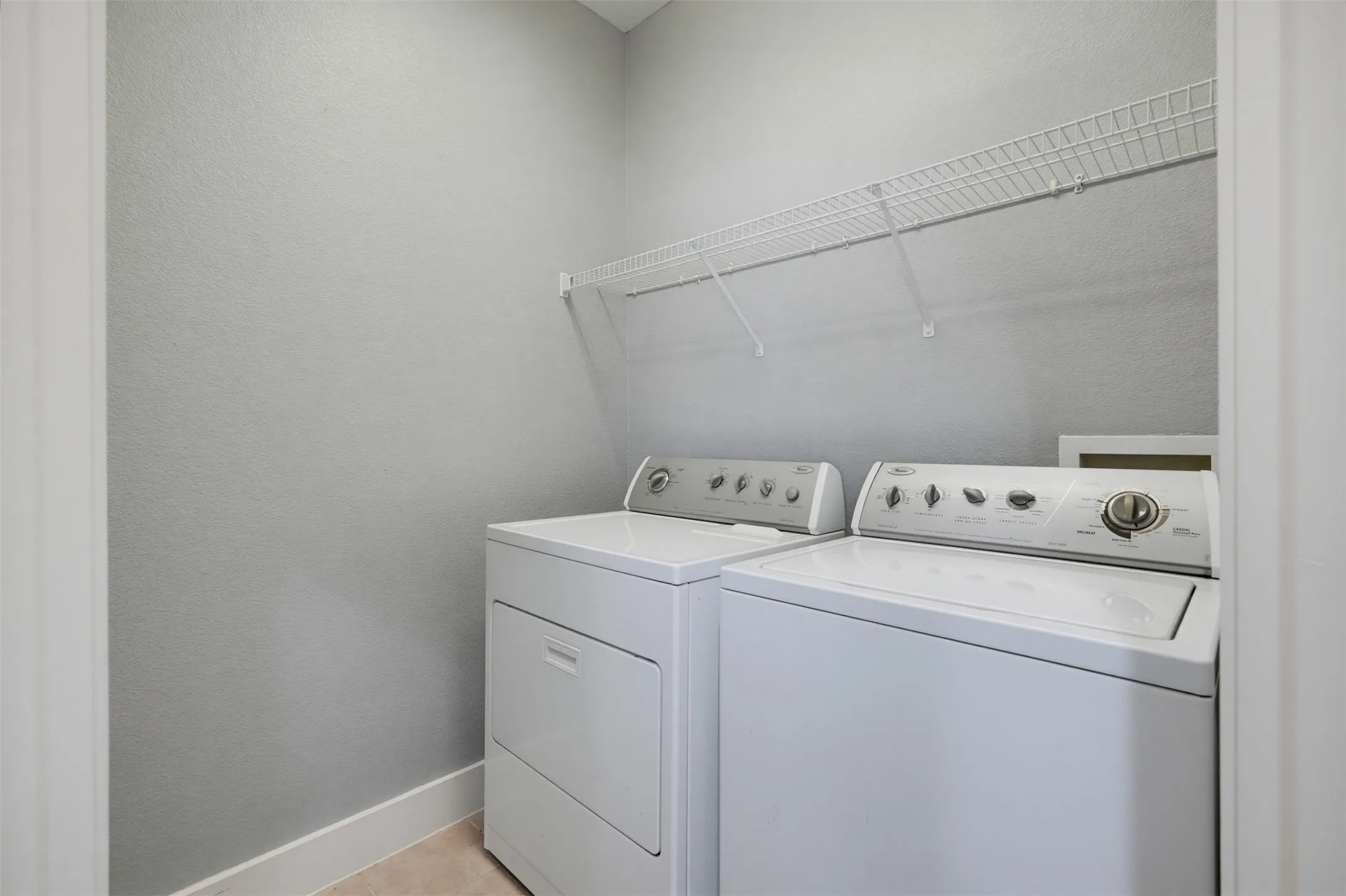 Dedicated laundry area featuring a white washer and dryer set, overhead wire shelving, light gray wall finish, and neutral flooring