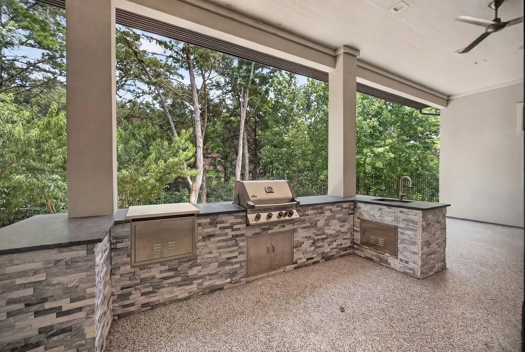 Covered outdoor kitchen featuring stacked stone veneer, built-in gas grill, stainless steel cabinetry, and an integrated sink with a gooseneck faucet