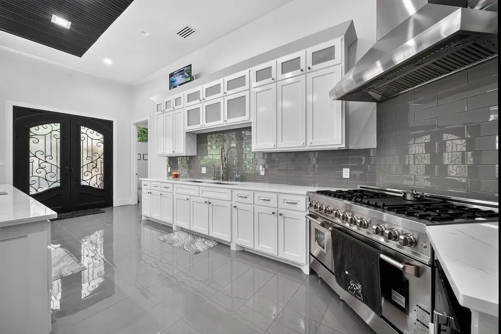 Gourmet kitchen featuring white shaker cabinetry, an integrated stainless steel range with a professional hood, gray subway tile backsplash, and light-toned countertops