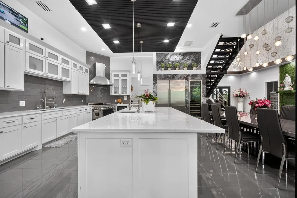 Gourmet kitchen and dining area featuring a spacious island, integrated stainless steel appliances, white cabinetry with glass inserts, and dark tile flooring