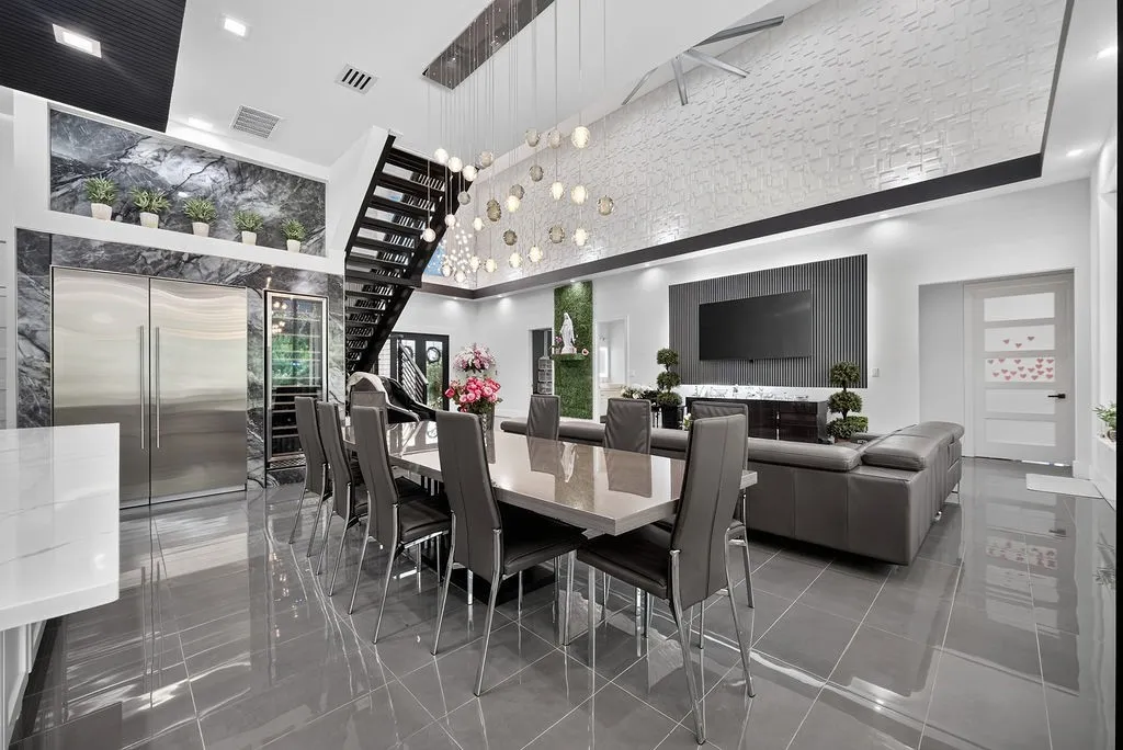 Spacious open-concept interior featuring high-gloss floor tile, a modern floating staircase, striking stone accent walls, a large built-in stainless steel refrigerator, and an integrated wine cooler