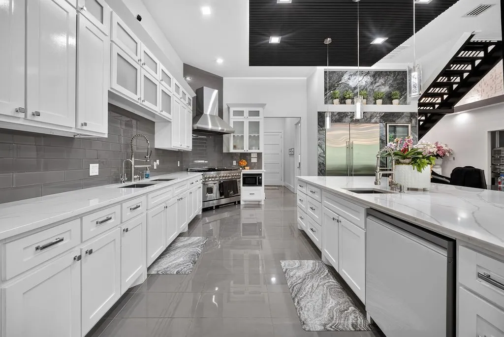Spacious kitchen featuring extensive white cabinetry, light countertops, a large center island with an undermount sink, stainless steel appliances, and grey subway tile backsplash