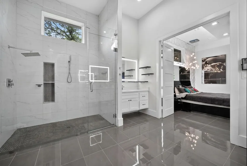 Spacious bathroom featuring a glass-enclosed shower with rain showerhead, white marble-look wall tile, a built-in shower niche, and a vanity with an illuminated mirror