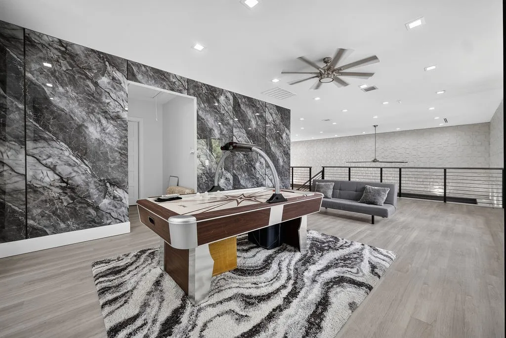Spacious room featuring a striking dark marble-patterned accent wall, light wood-finish flooring, and recessed lighting