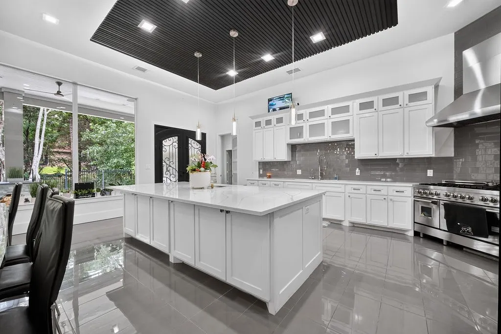 Spacious kitchen featuring a large central island with a white countertop, white cabinetry, a stainless steel range with a professional hood, and polished tile flooring