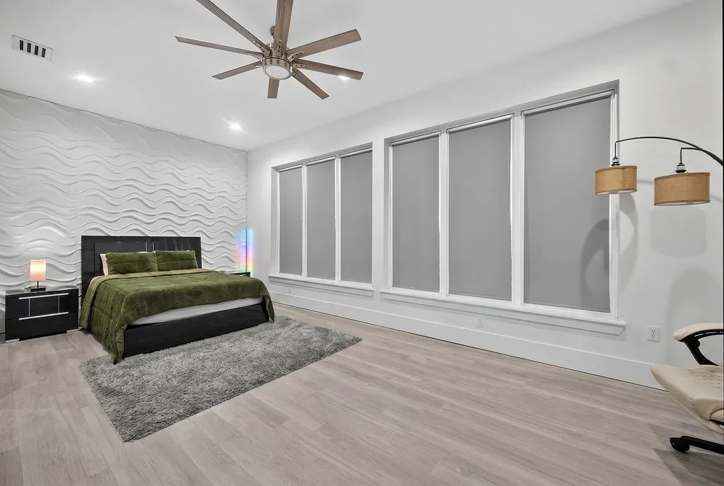 Bedroom featuring a textured accent wall, light wood-finish flooring, and a multi-blade ceiling fan