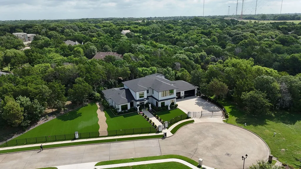 Contemporary-style residence with a dark roof and light-colored siding, featuring a circular driveway, a gated entry, and an expansive manicured lawn
