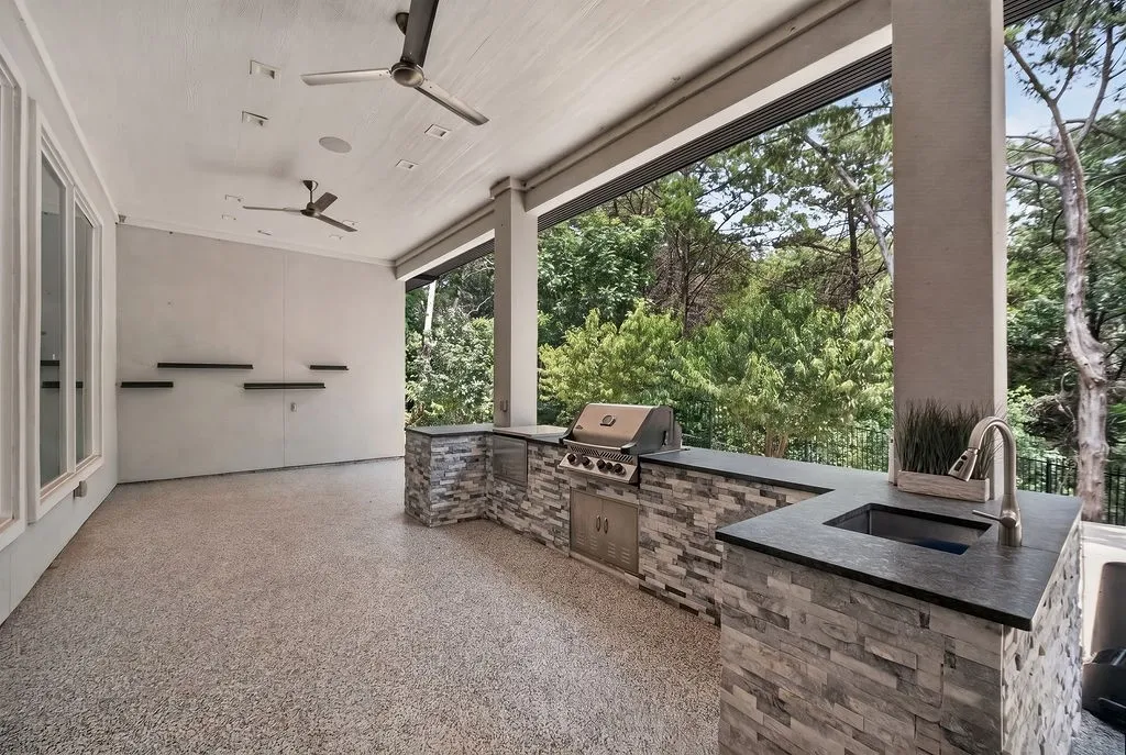Covered outdoor living area featuring a built-in kitchen with a grill, sink, and stone-clad cabinetry
