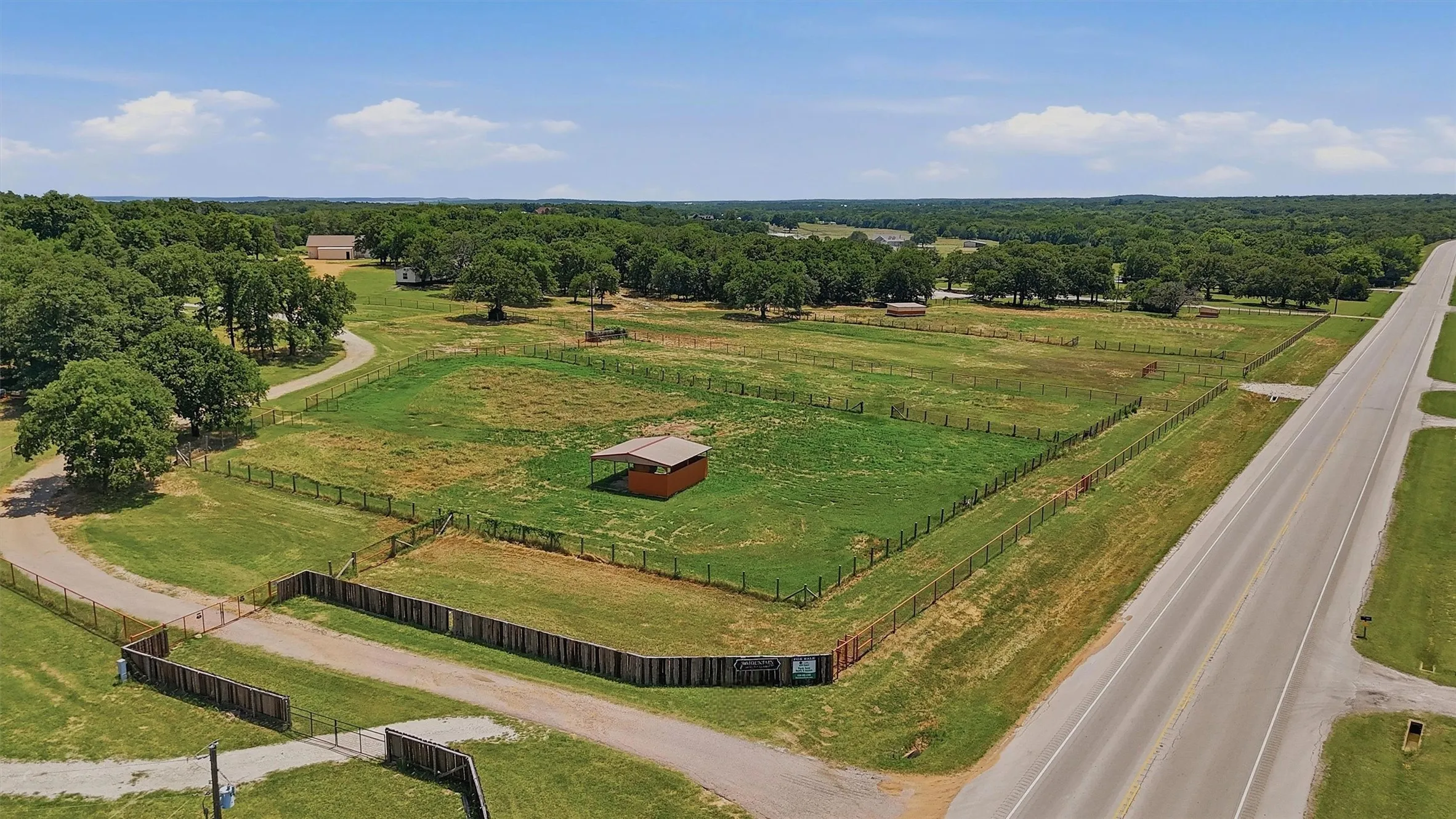 Expansive acreage featuring multiple fenced paddocks, a roadside location, a private drive, mature trees, and an open-sided shelter