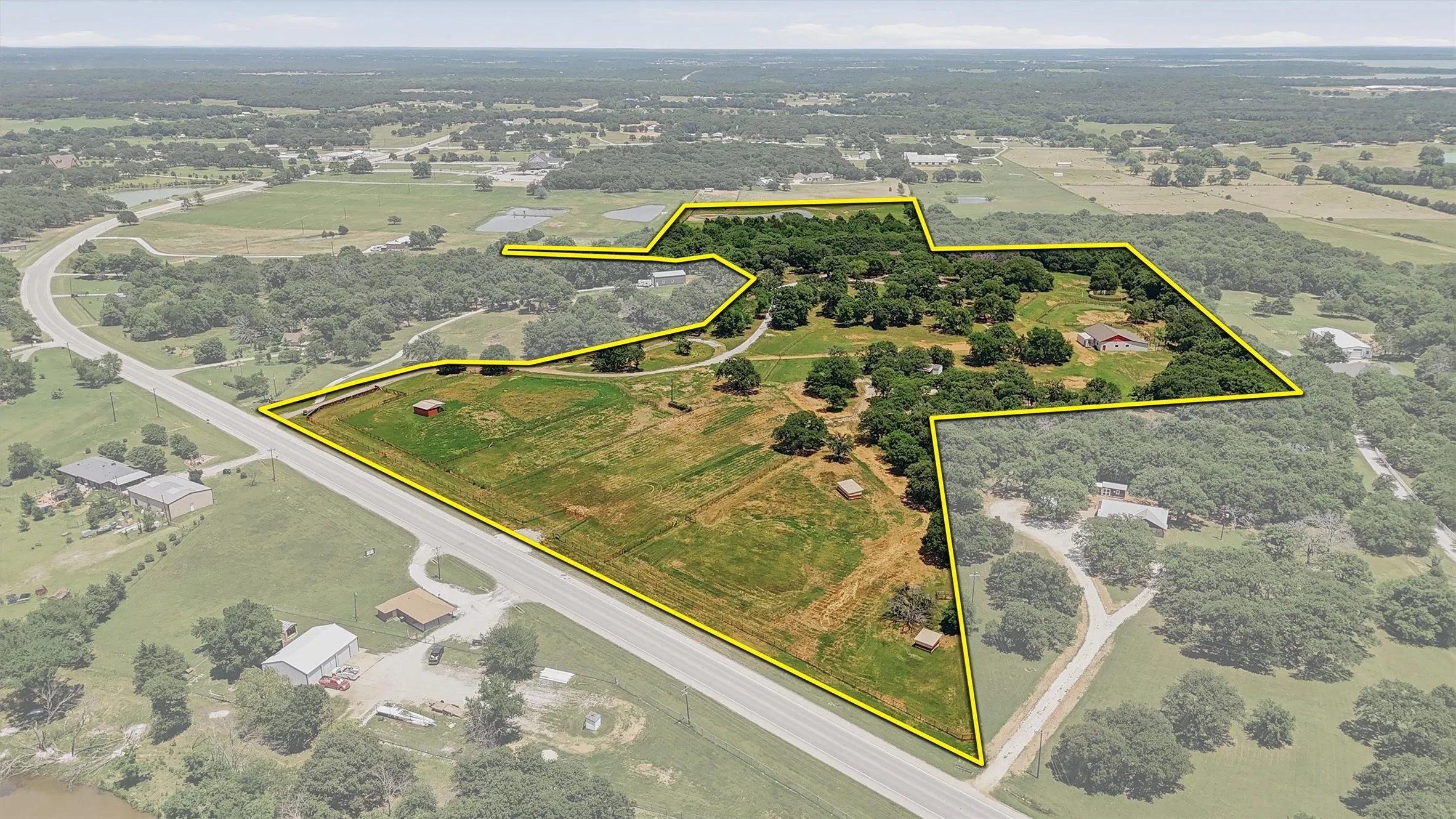 Expansive rural property featuring a primary residence with a red roof, a secondary structure, cleared acreage, mature trees, and direct road frontage