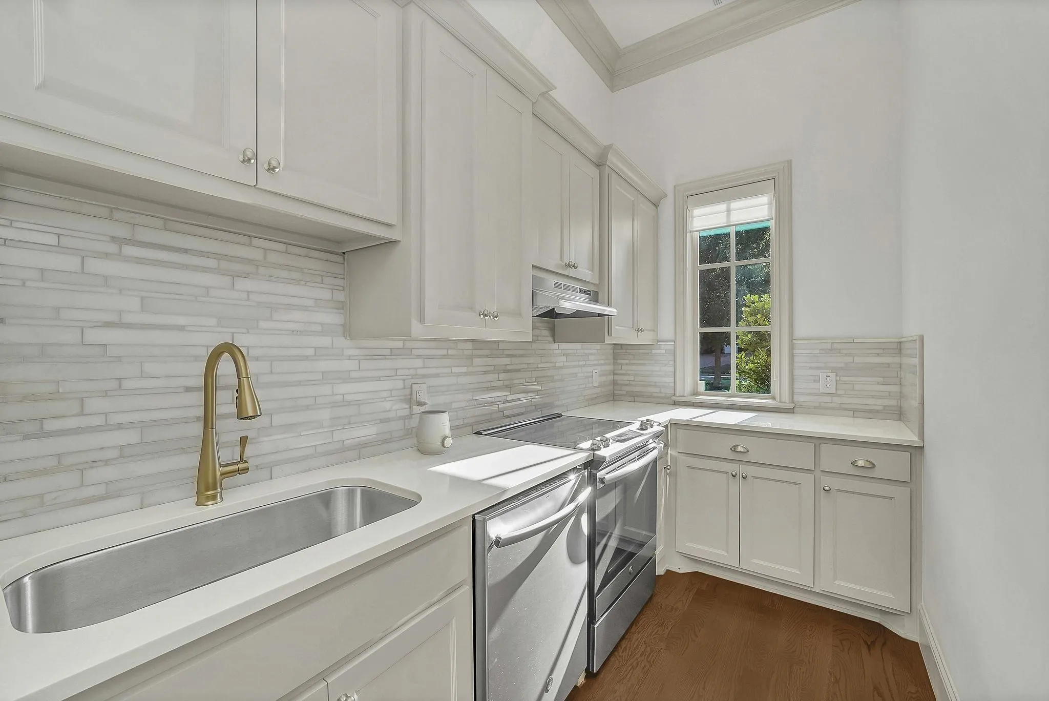 Modern kitchen featuring white shaker-style cabinetry, a stainless steel undermount sink with a brass-finish faucet, and white quartz countertops