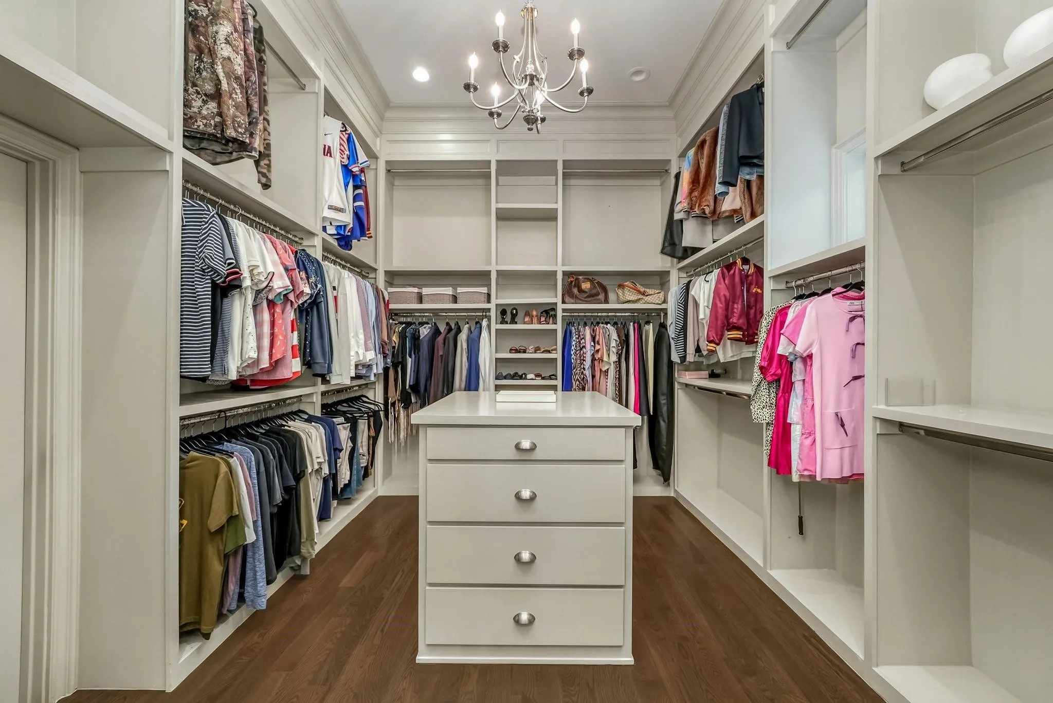 Custom walk-in closet featuring built-in cabinetry, varied hanging rods, open shelving, and a central island with drawers