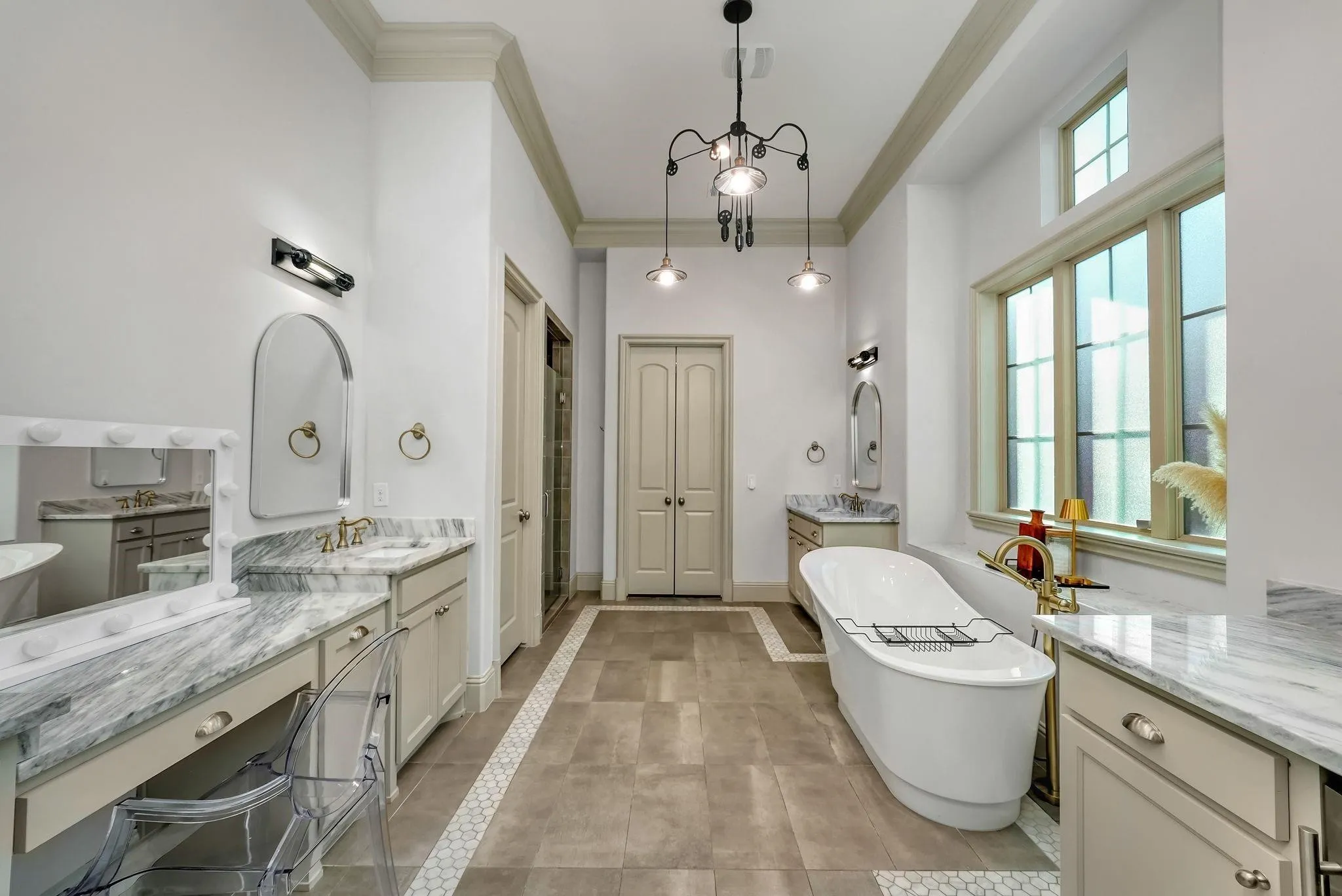 Spacious bathroom featuring a freestanding soaking tub, dual vanity with stone countertops, tiled flooring with mosaic accents, and a large window providing natural illumination