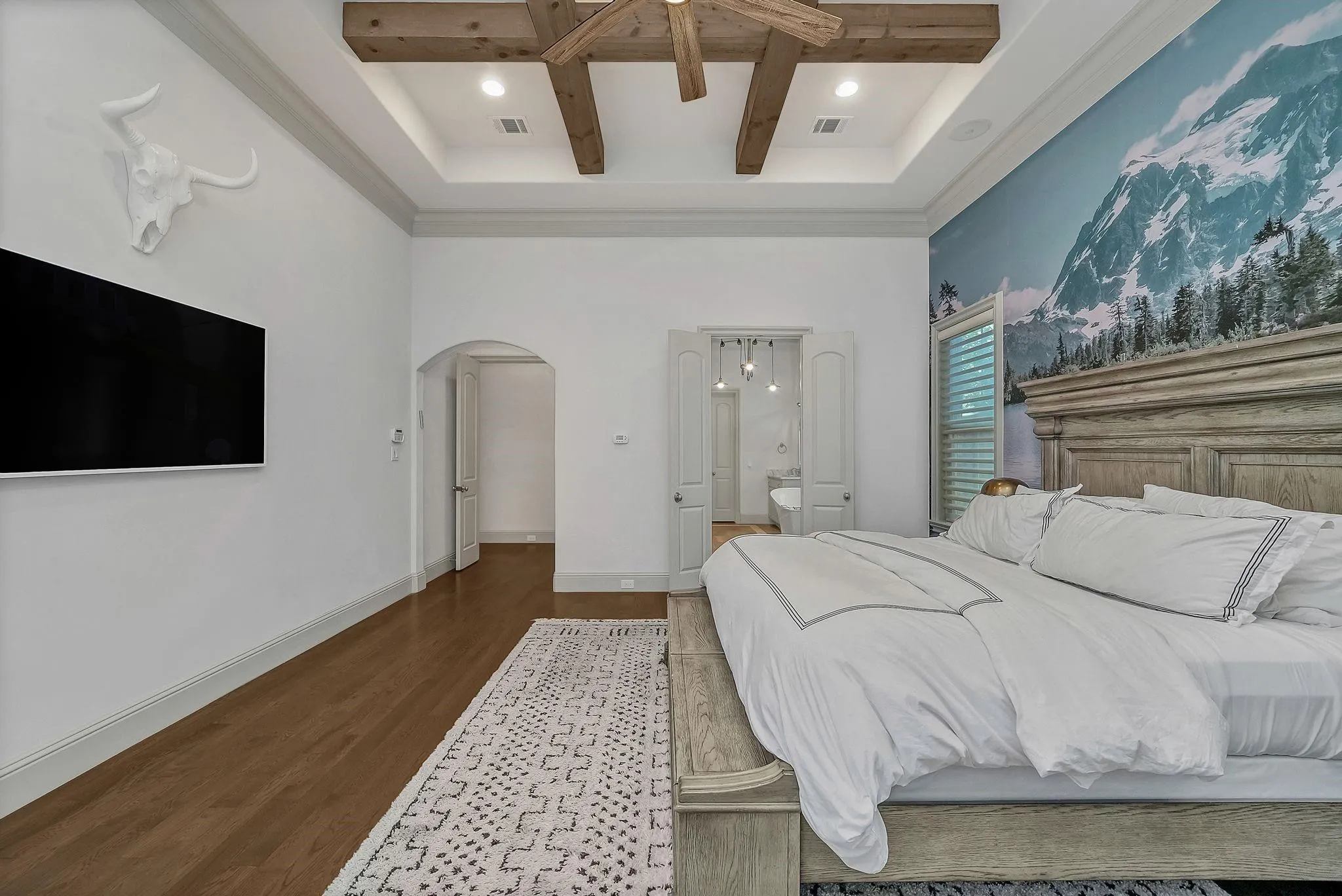 Bedroom featuring a tray ceiling with exposed wood beams, wood-finish flooring, and a decorative accent wall